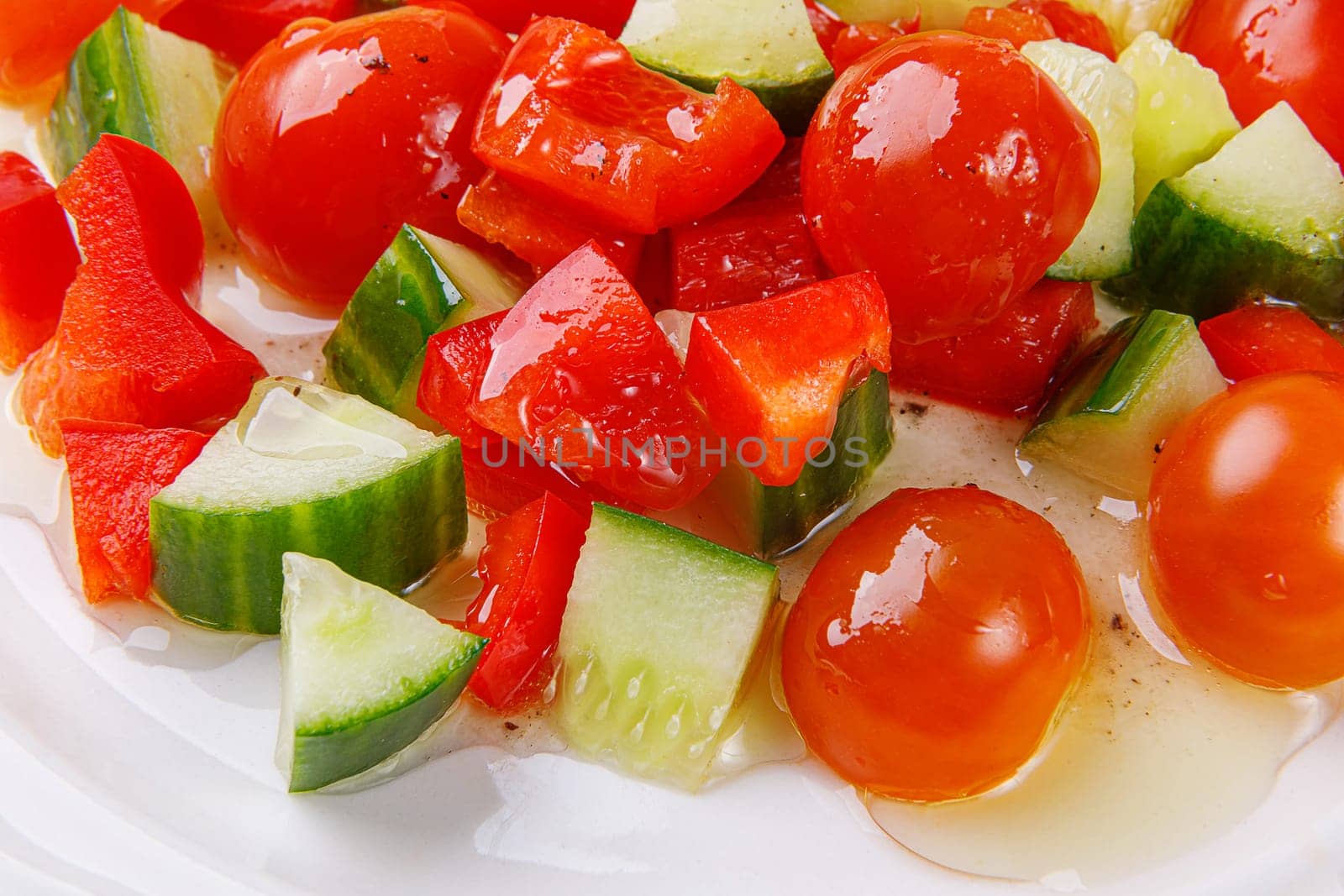 Salad of cucumbers, cherry tomatoes, peppers and dressing in a plate on a white wooden background