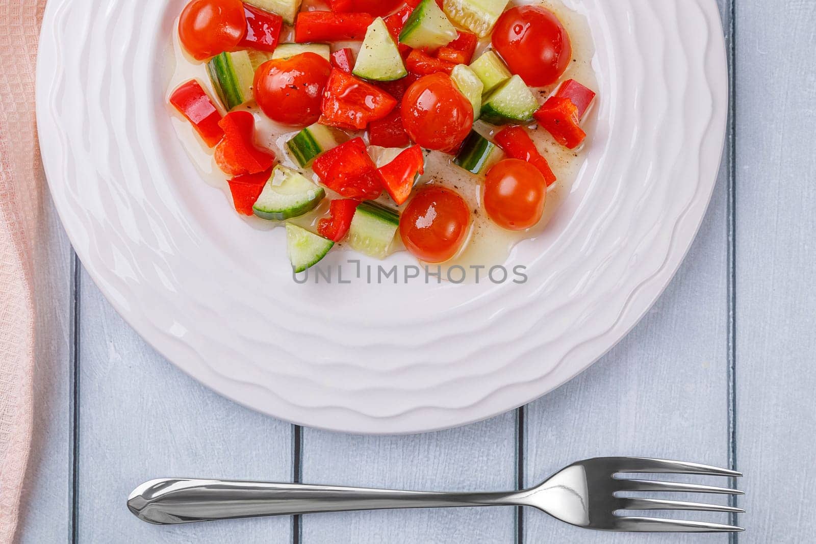 Salad of cucumbers, cherry tomatoes, peppers and dressing in a plate on a white wooden background