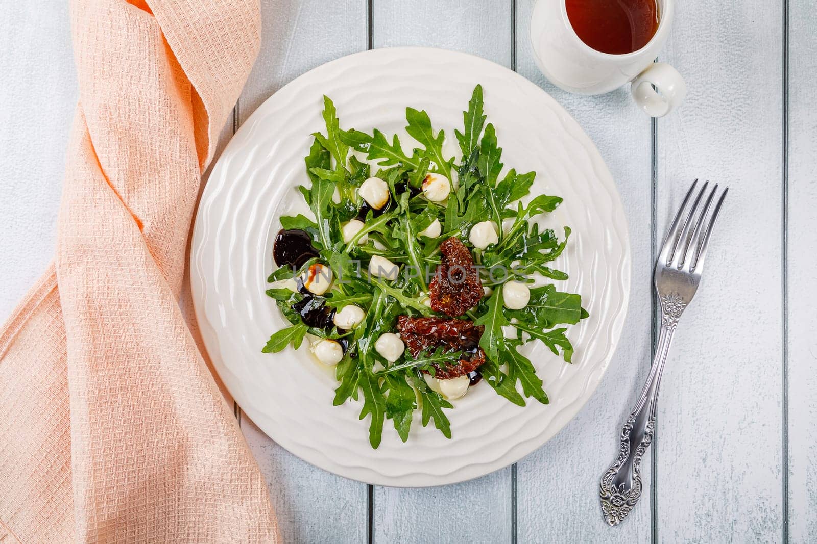 Fresh salad with arugula, mozzarella cheese, sun-dried tomato and white wood dressing