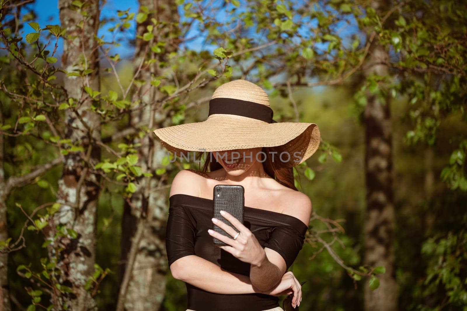 Beautiful happy woman in hat with phone in hand in summer by EkaterinaPereslavtseva