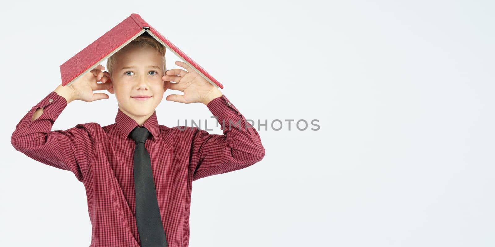 The schoolboy put an open book on his head and covered his ears with his fingers, isolated background. Education concept