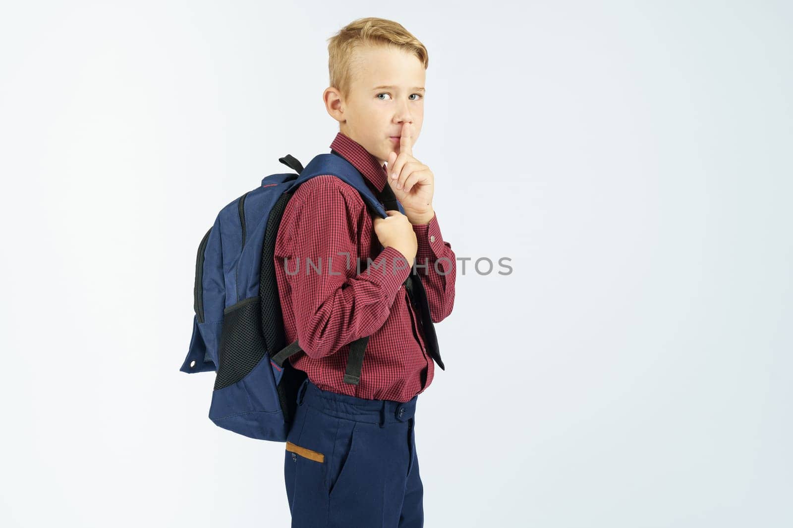 A schoolboy holds a school backpack and shows a gesture with his hand - be quiet. Education concept