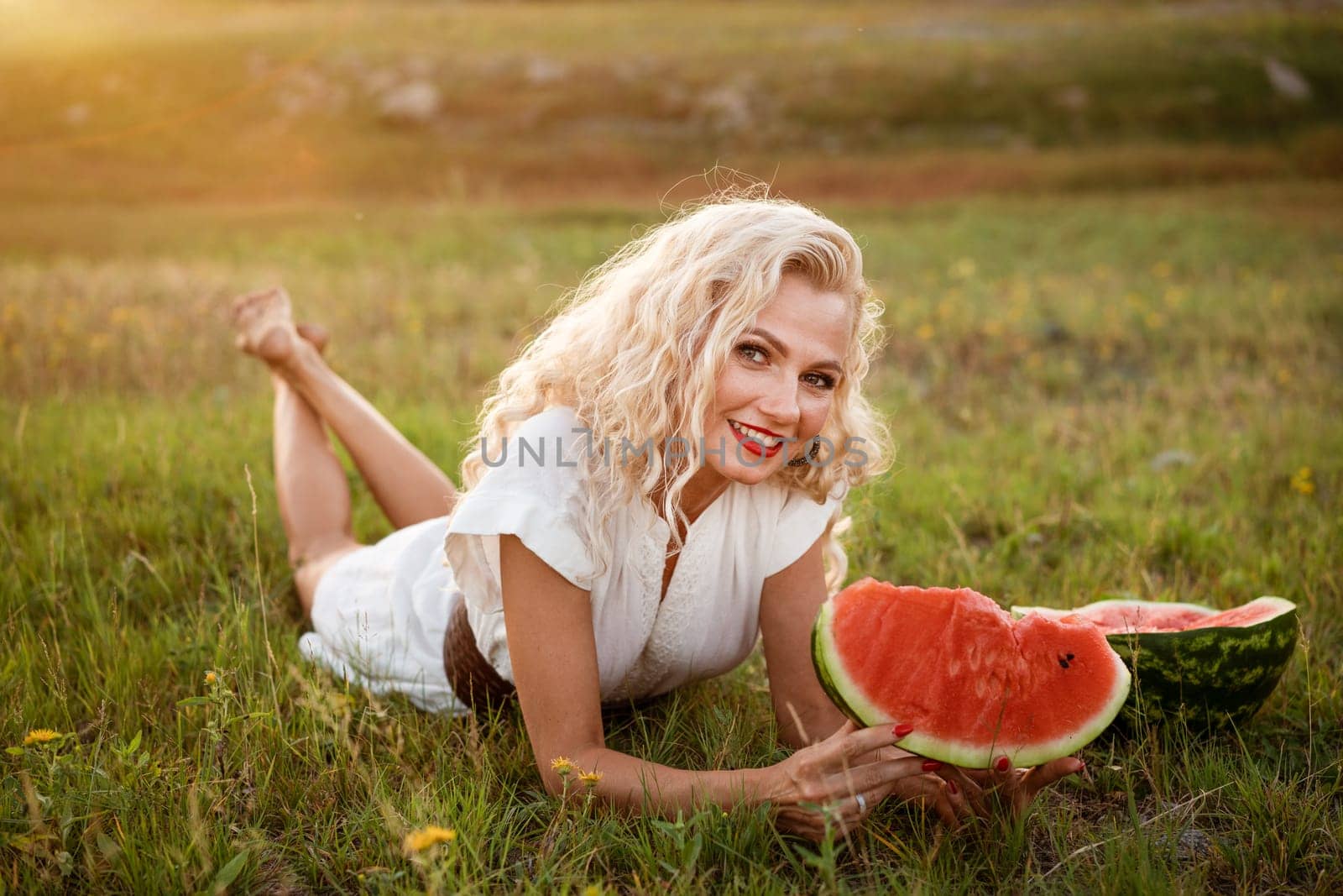 Young woman walking in a park outdoors on a sunny day enjoying summer and dreaming. Cheerful girl holding a piece of watermelon in front of her face. Summer vacation concept
