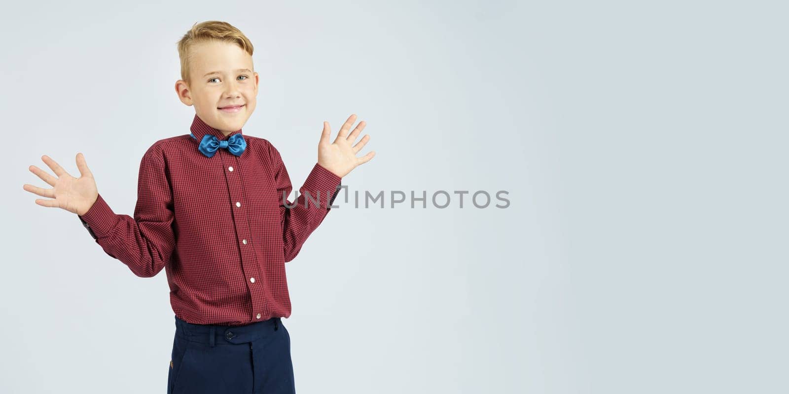 A portrait of a schoolboy who raised his hands in surprise and joy. Isolated background. Education concept.