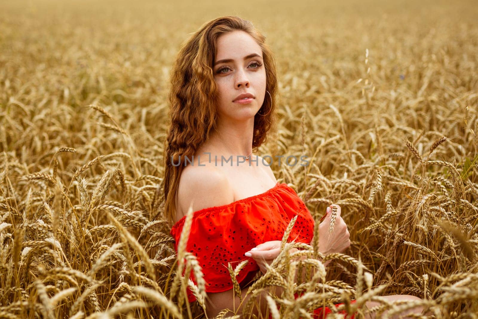 Style redhead girl in red clothes tay on yellow wheat field Caucasian real girl. Portrait of a beautiful young woman on a natural natural background. Natural cosmetics concept.