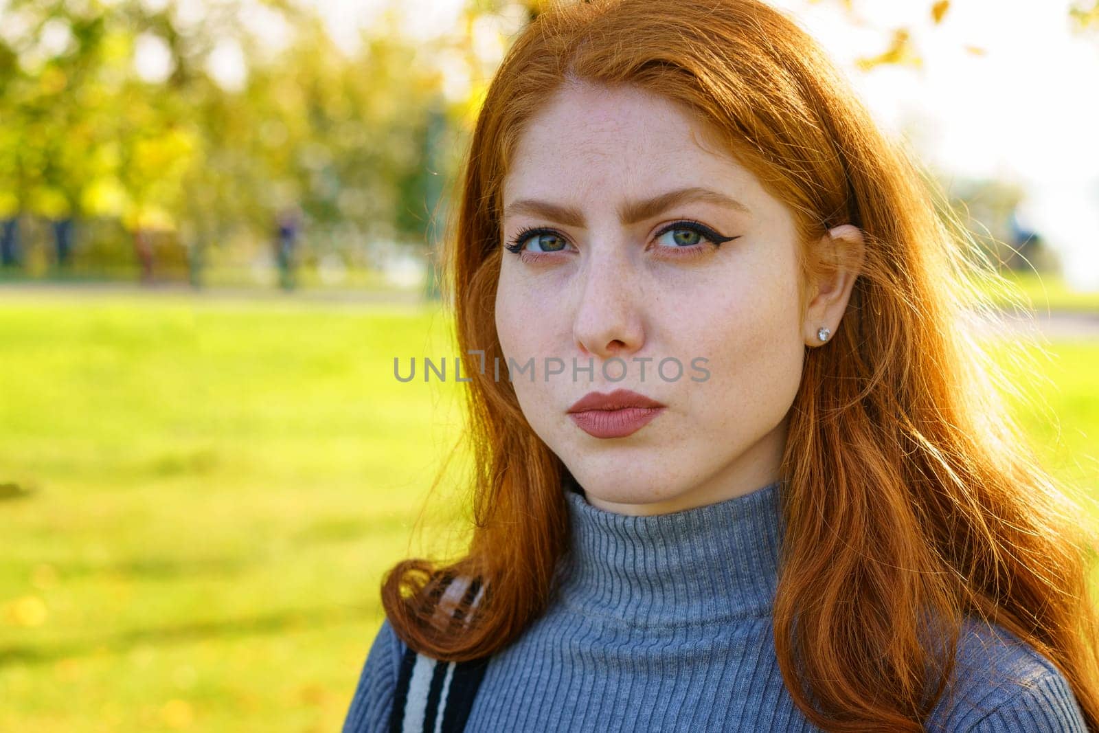 Closeup female portrait of a red-haired Caucasian woman, with makeup with green eyes looking at the camera on a natural background on a sunny day