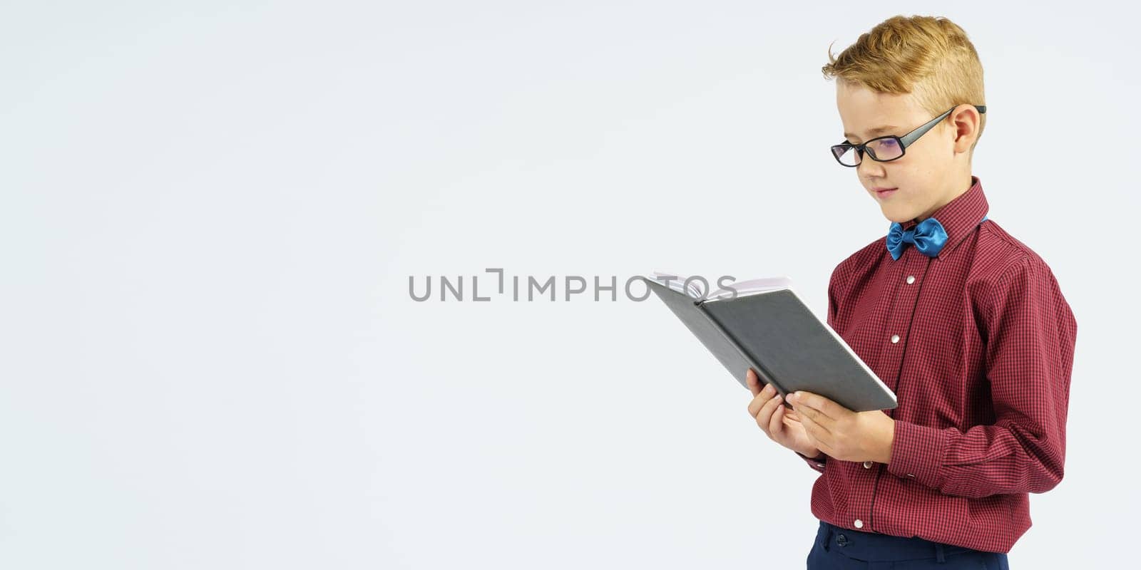 A schoolboy with glasses reads a book he holds in his hands. Isolated background. Education concept