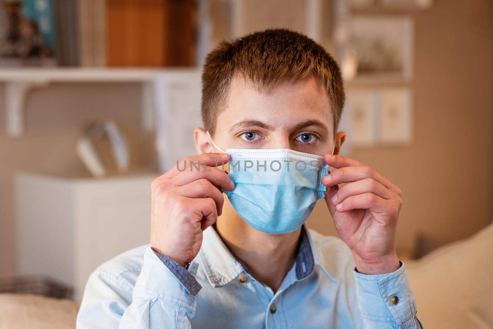 young guy sitting on the couch wearing a medical mask by EkaterinaPereslavtseva