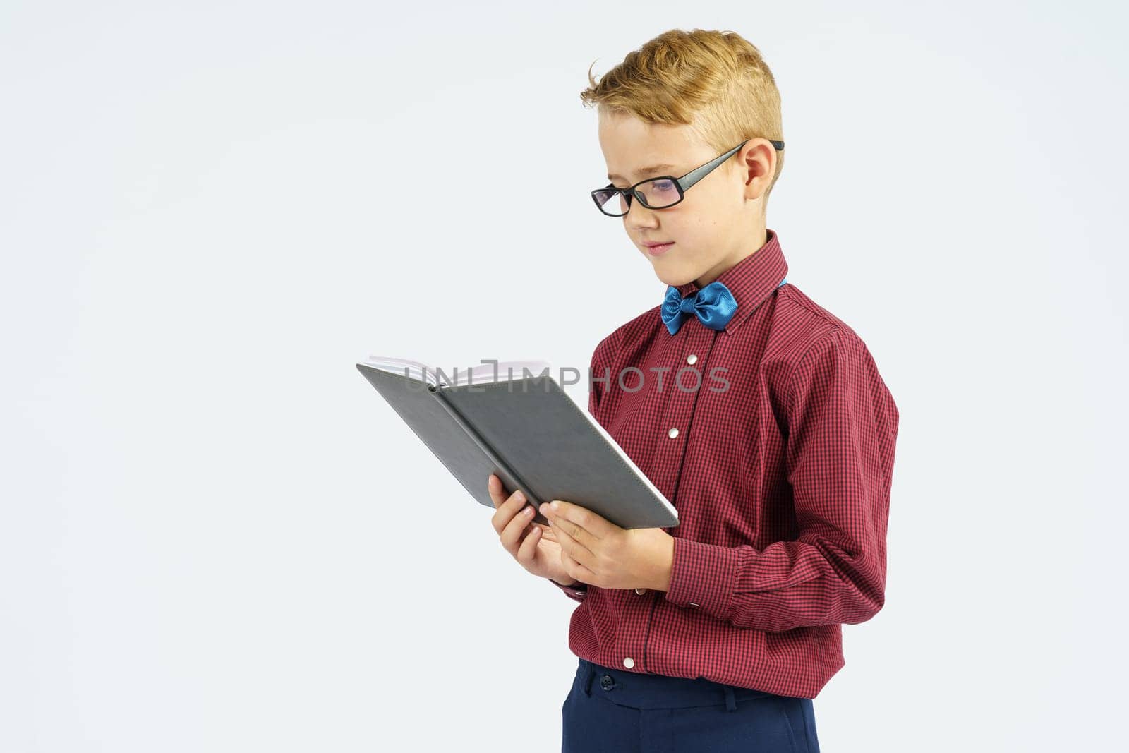 A schoolboy with glasses reads a book he holds in his hands. Isolated background. Education concept