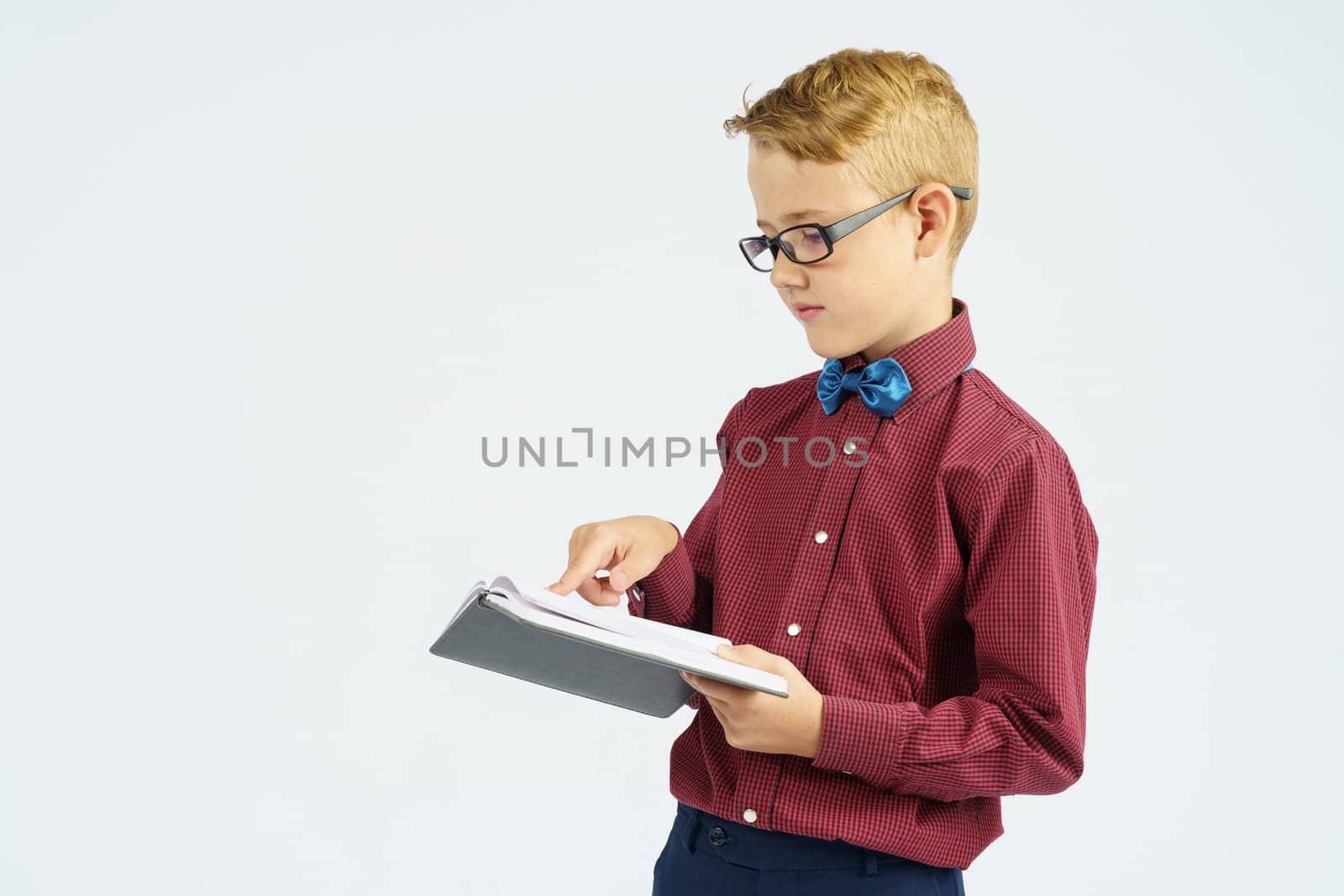 A schoolboy with glasses reads a book he holds in his hands. Isolated background. Education concept