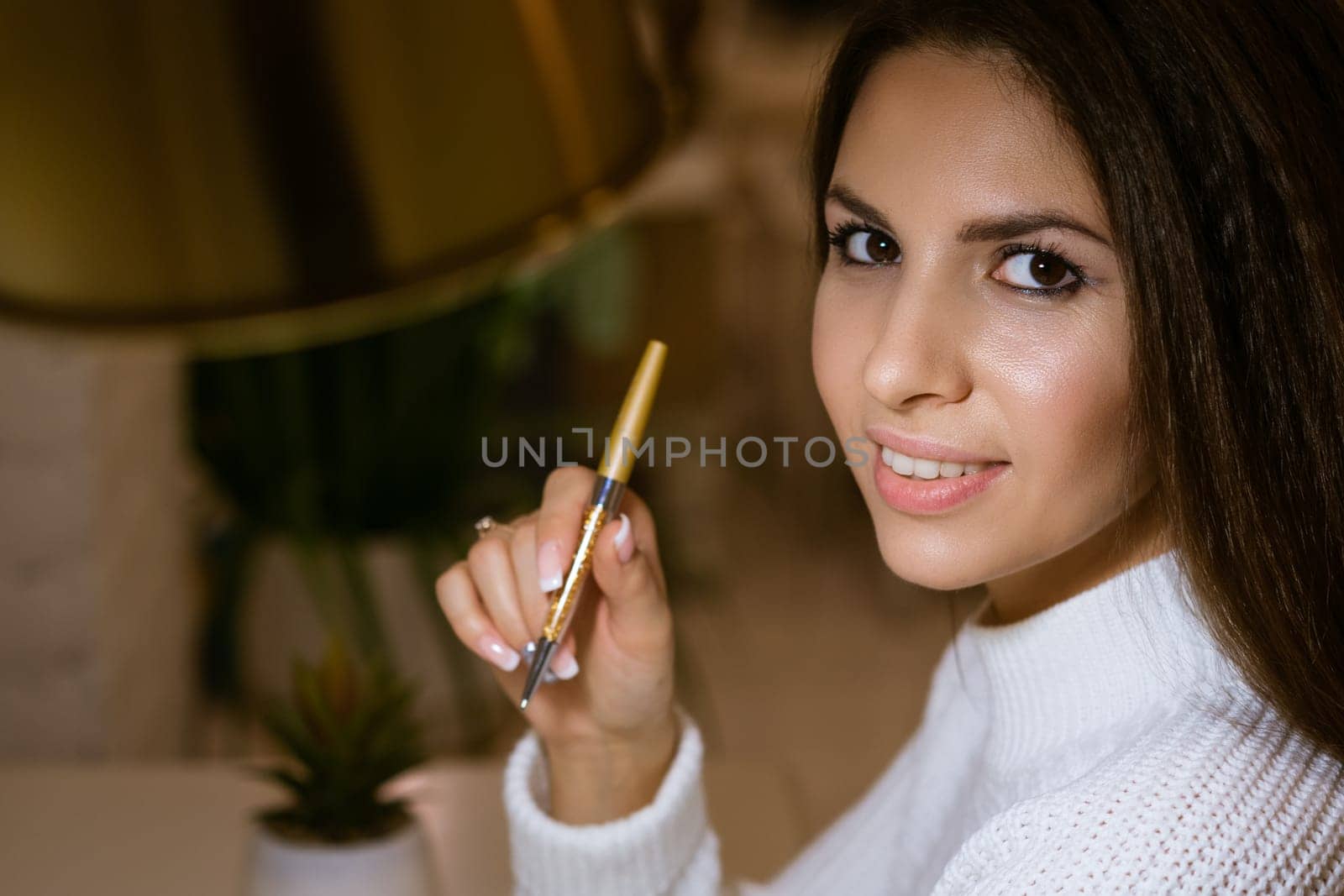 beautiful young woman in a white sweater with a pen in her hand sits pensive at the table