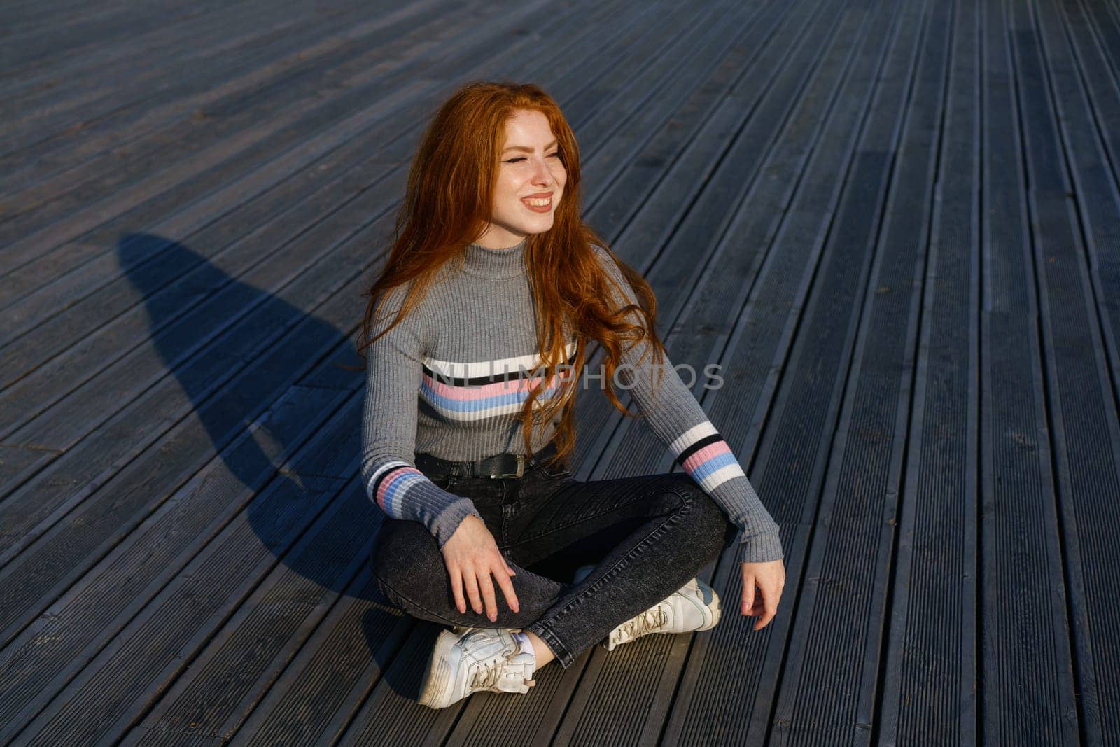 Happy young woman with red hair in the park on wooden flooring by EkaterinaPereslavtseva