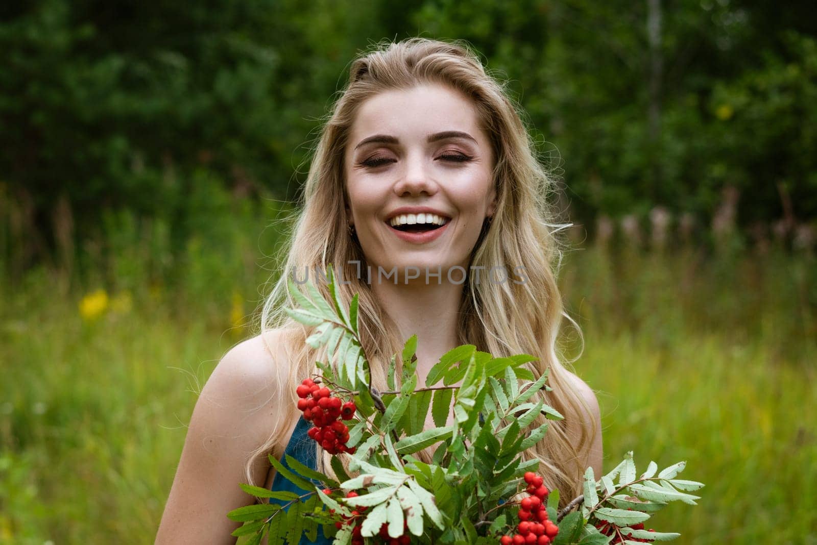 Portrait of a young beautiful blonde woman with a bouquet of rowan berries in nature close-up