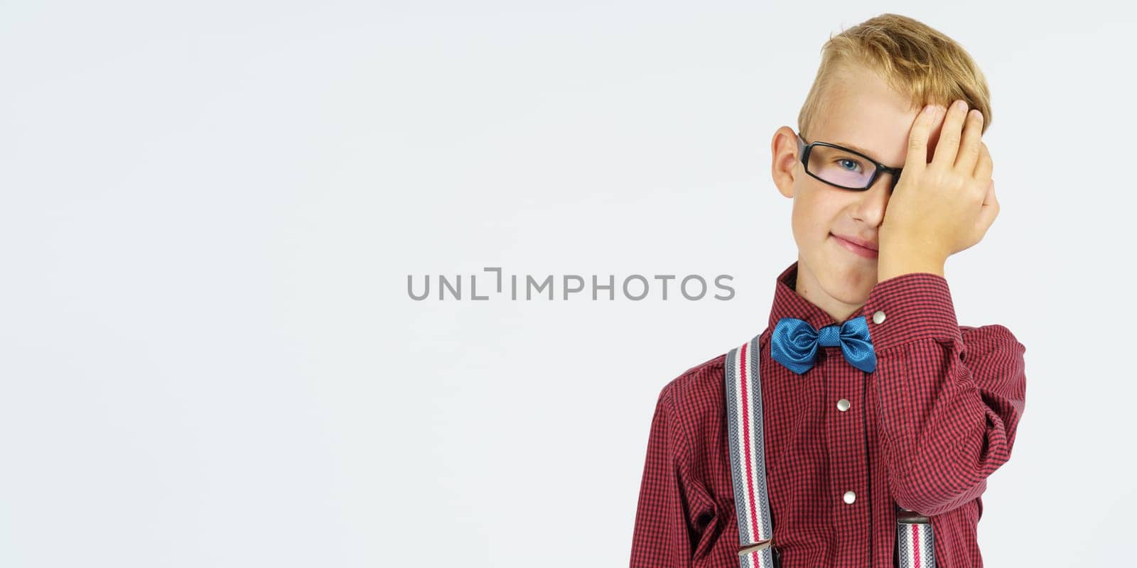 Portrait of a schoolboy who covered one eye with his hand. Isolated background. Education concept.