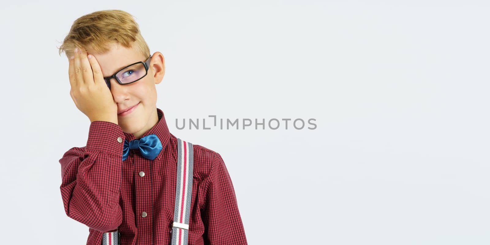 Portrait of a schoolboy who covered one eye with his hand. Isolated background. Education concept.