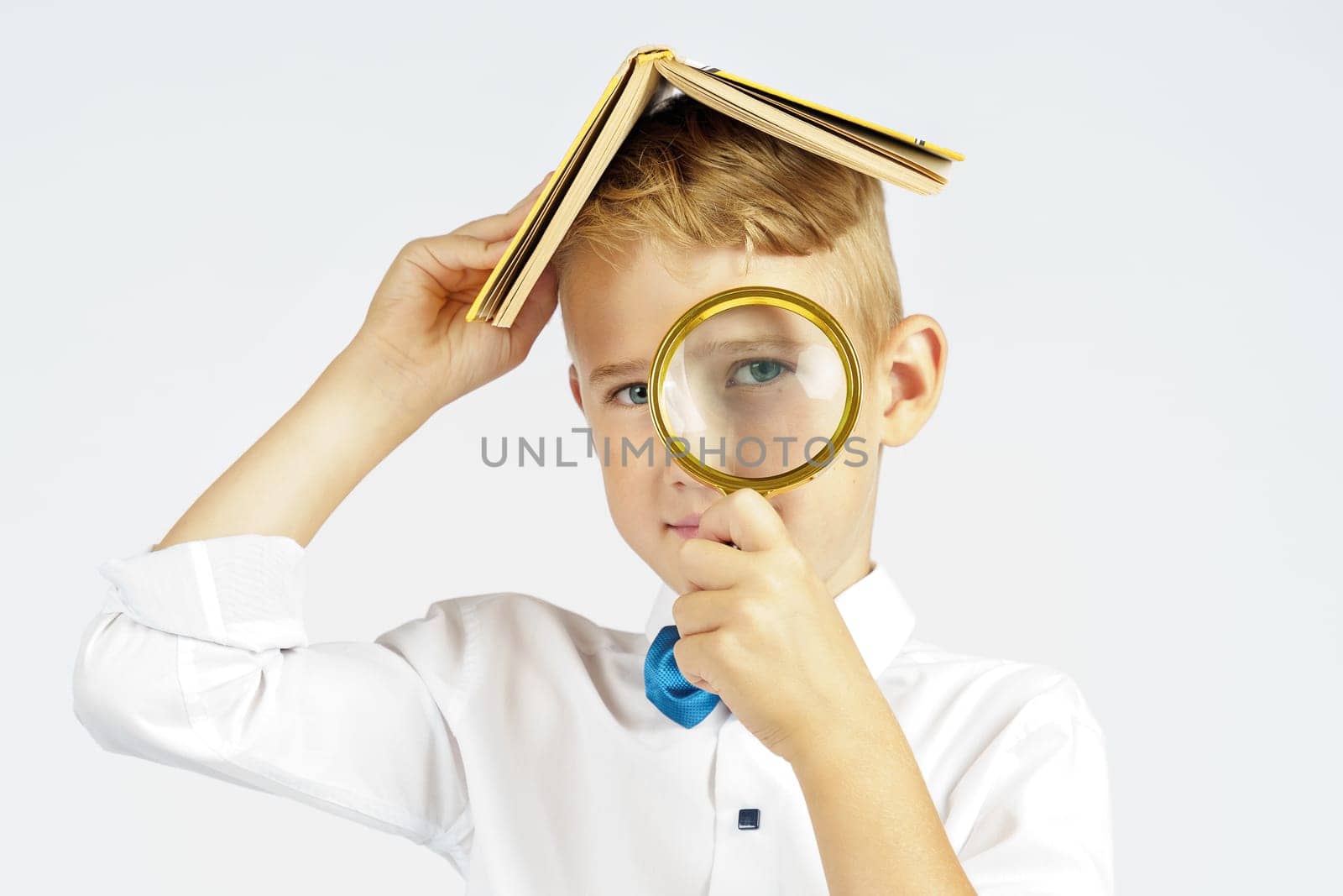 The schoolboy put the book on his head and looks through a magnifying glass. Isolated background. Education concept