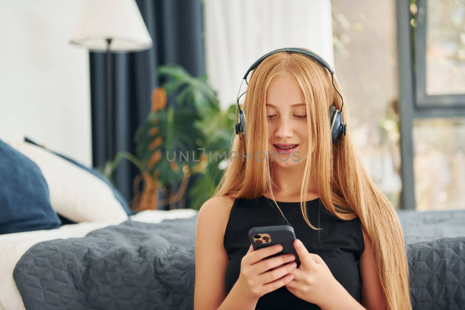 Listening to the music. Female teenager with blonde hair is at home at daytime.