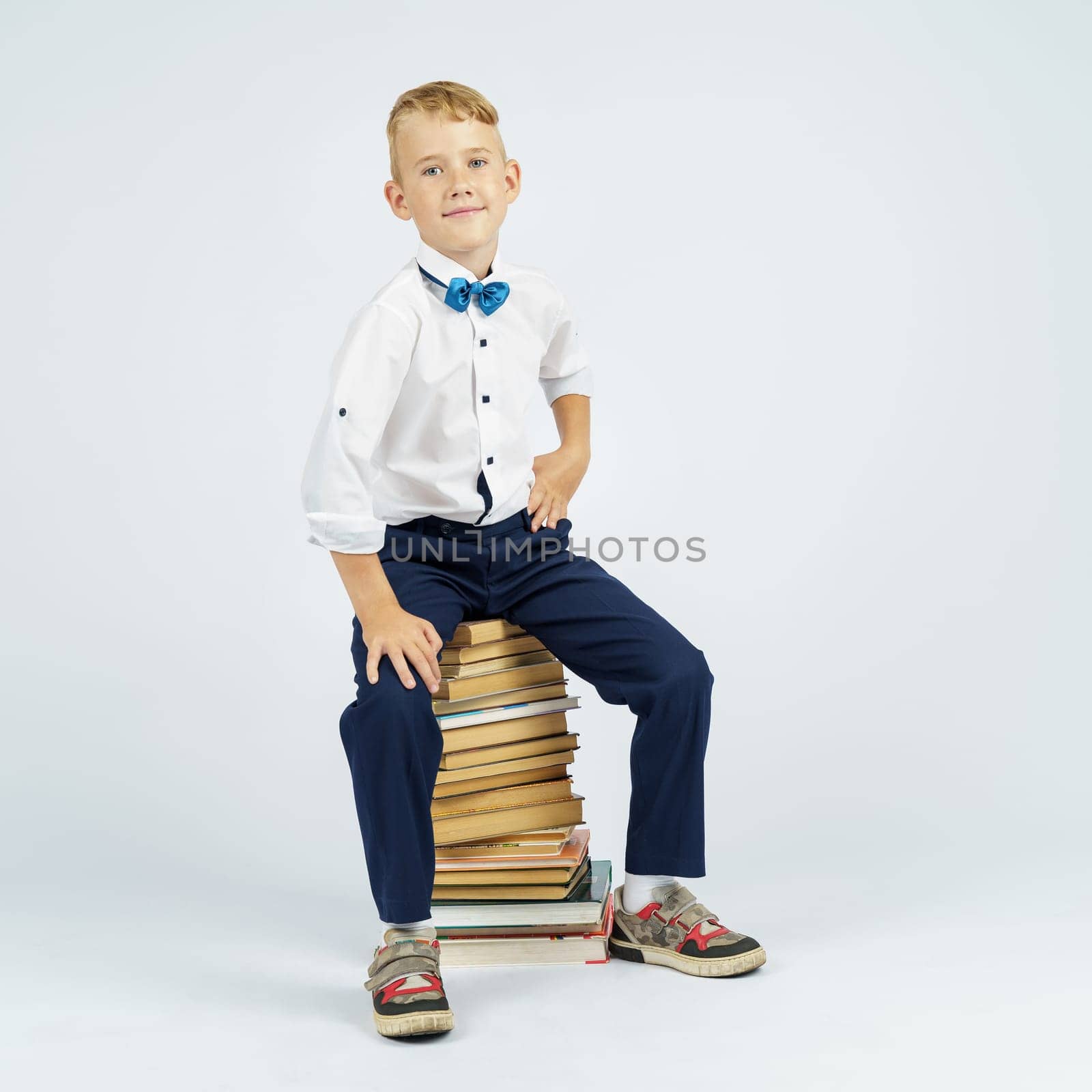 The schoolboy is sitting on books. Isolated background.