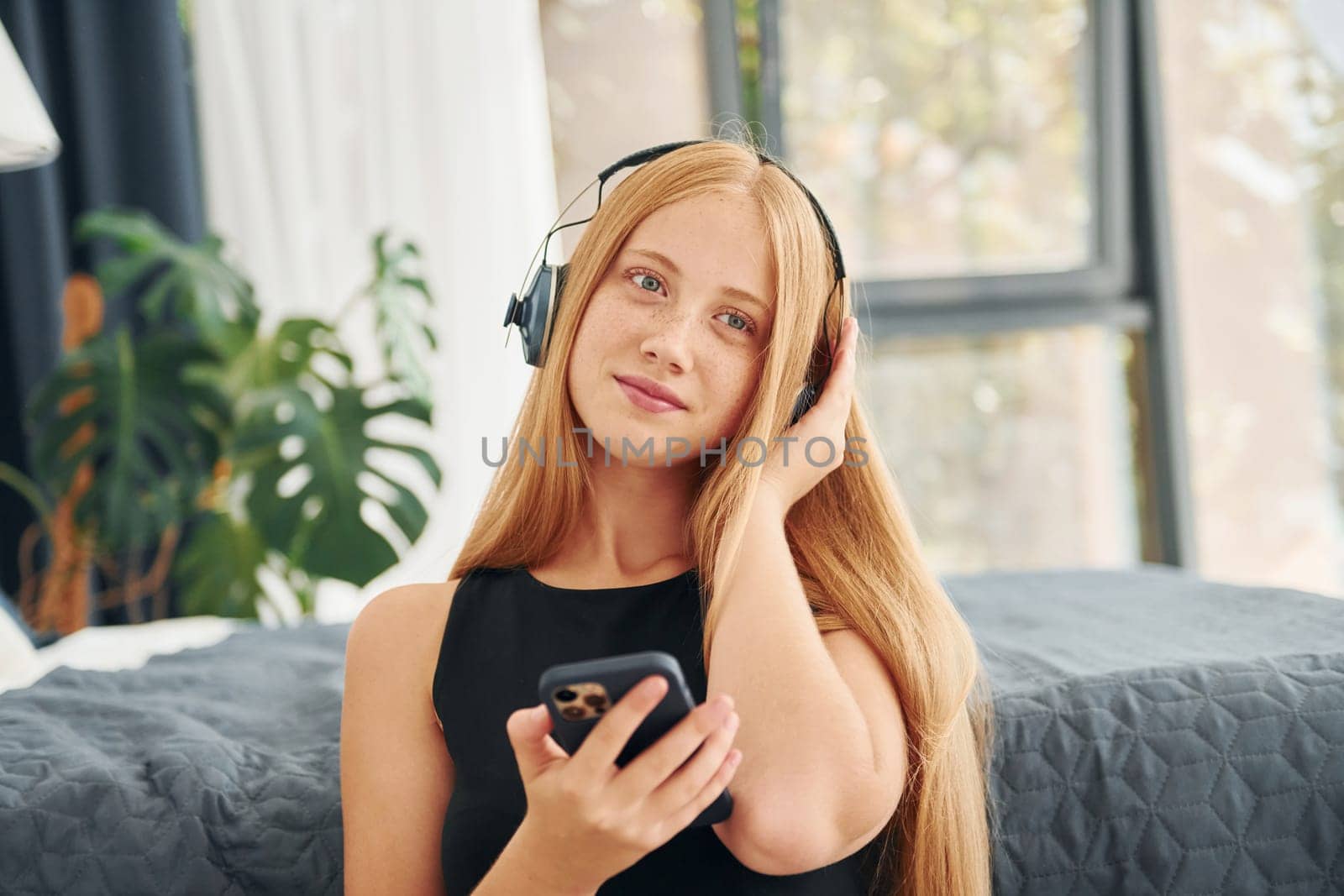 Listening to the music. Female teenager with blonde hair is at home at daytime.
