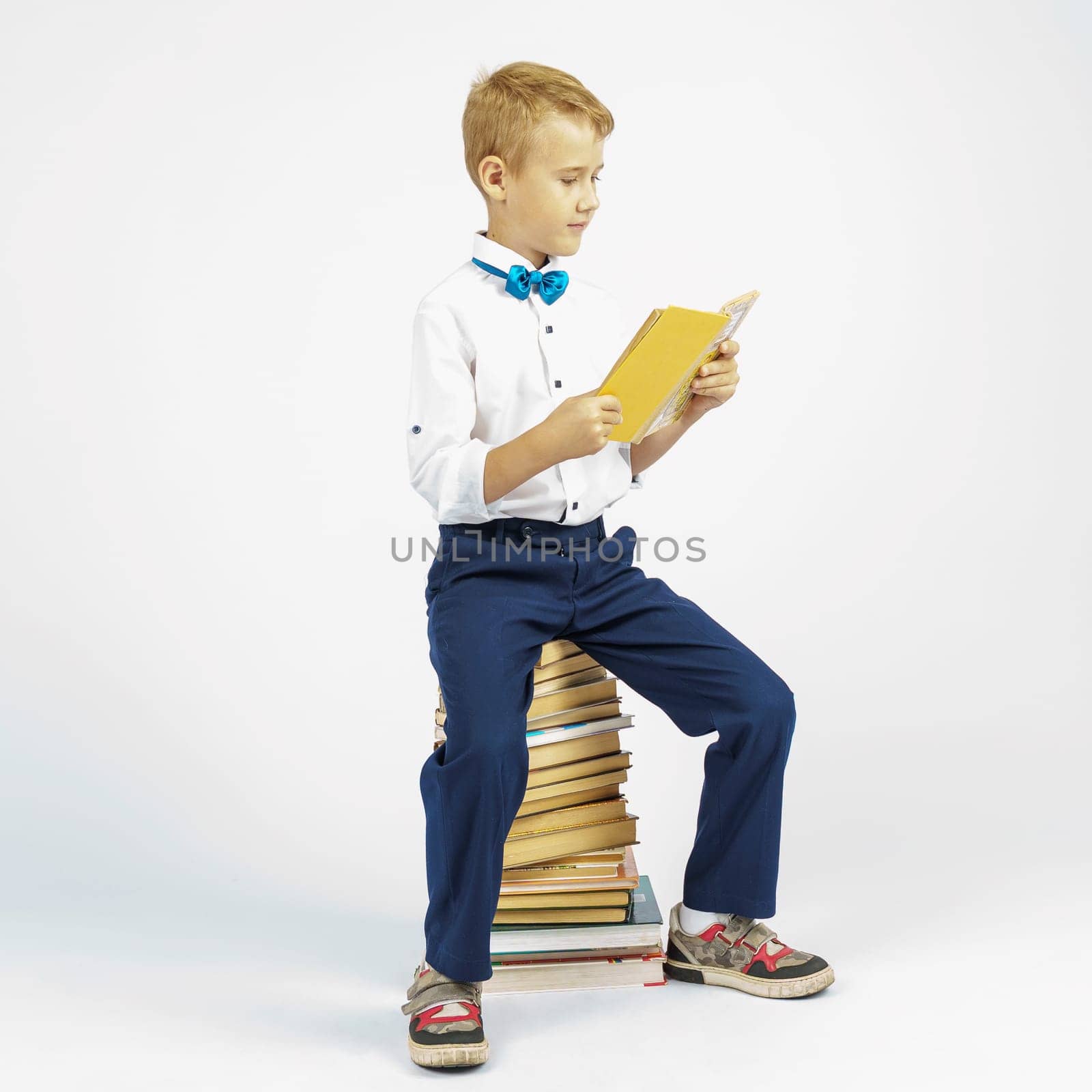 The schoolboy is sitting on books and reading a book. Isolated background. by Sd28DimoN_1976