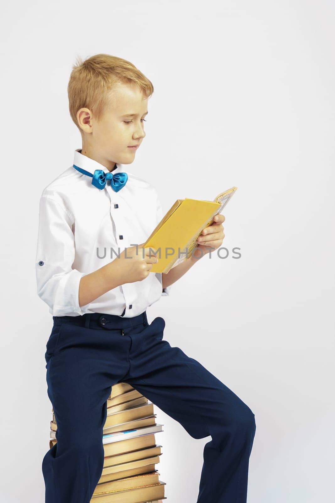The schoolboy is sitting on books and reading a book. Isolated background. Education concept