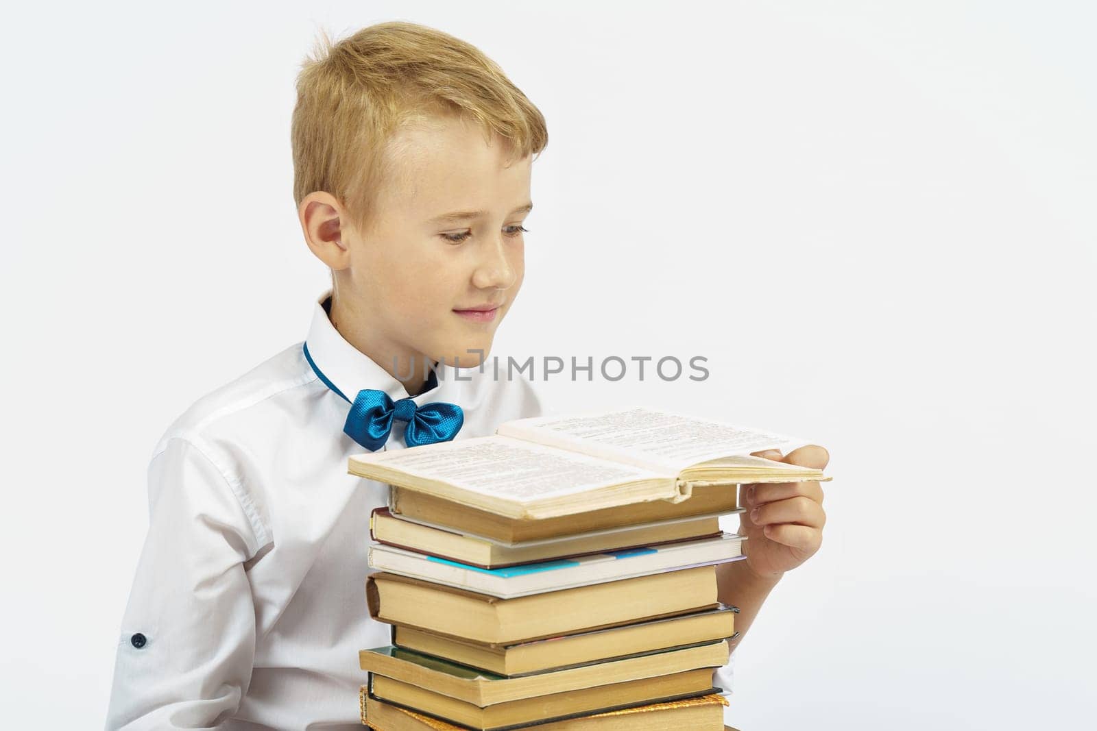 A schoolboy sits near a stack of books and reads. Isolated background. Education concept