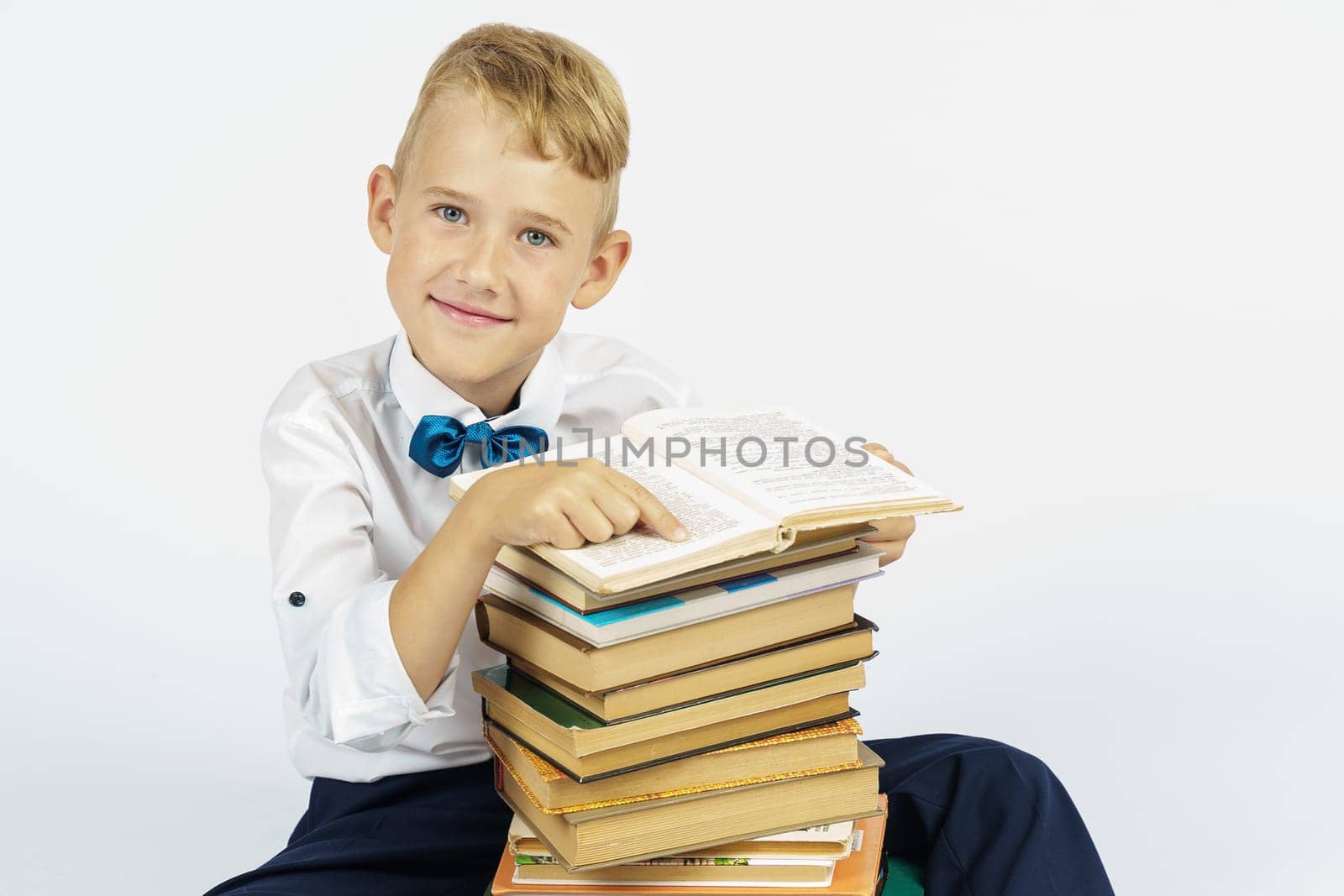A schoolboy is sitting near a stack of books and smiling while looking at the camera. Isolated background. Education concept