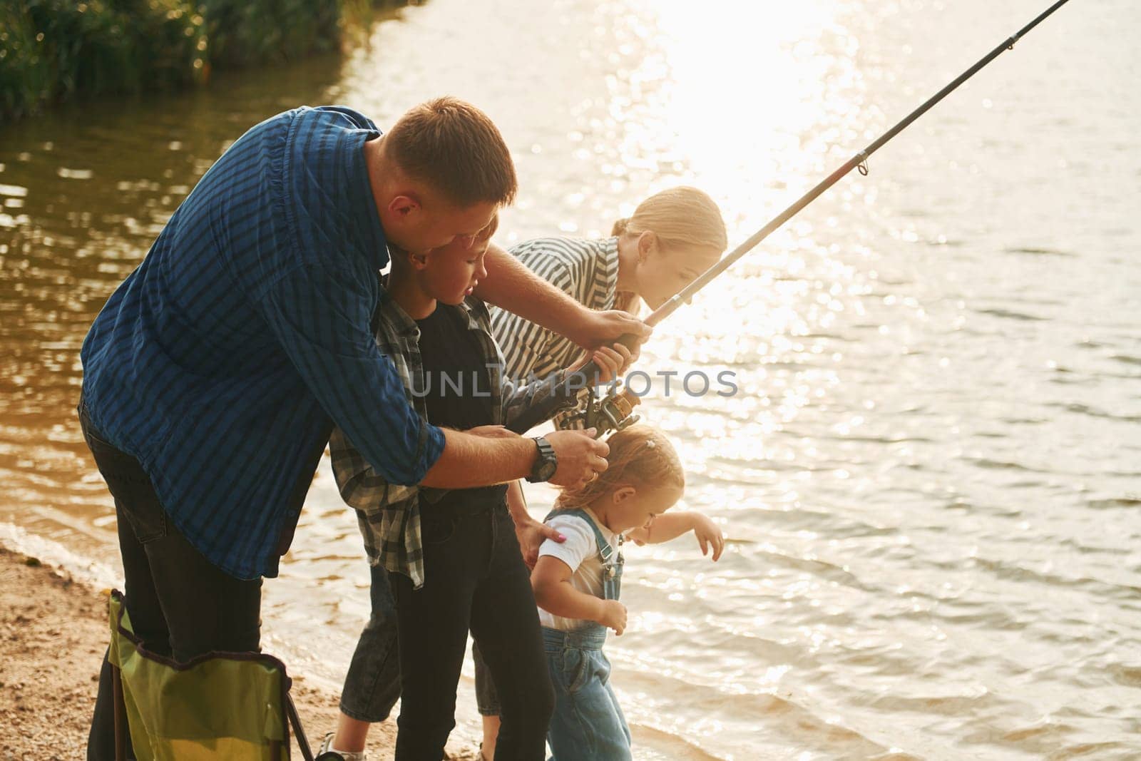 Learning to fishing. Father and mother with son and daughter together outdoors at summertime.