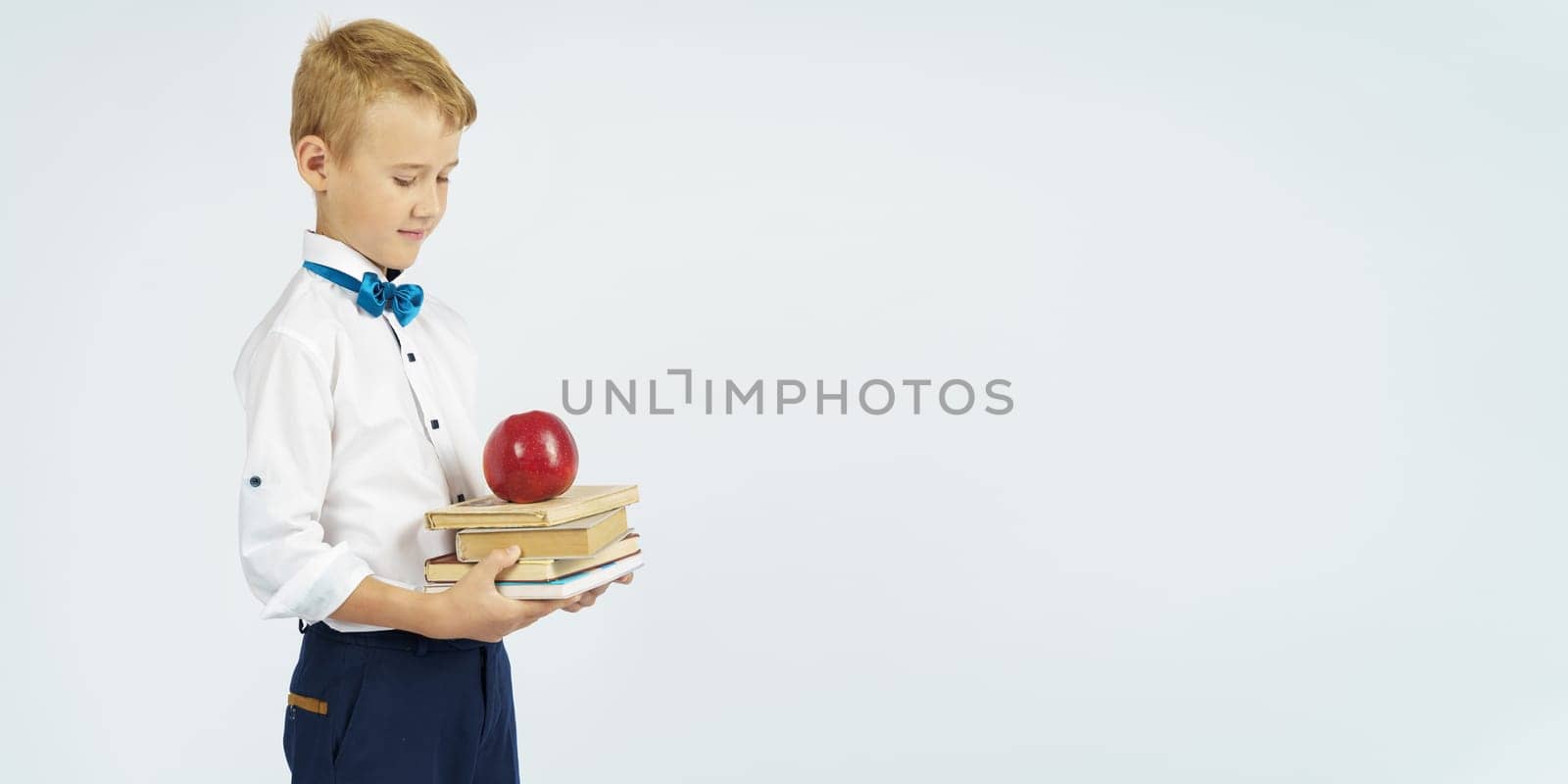 The schoolboy holds books and an apple in his hands. Looks at them. Isolated background. Education concept