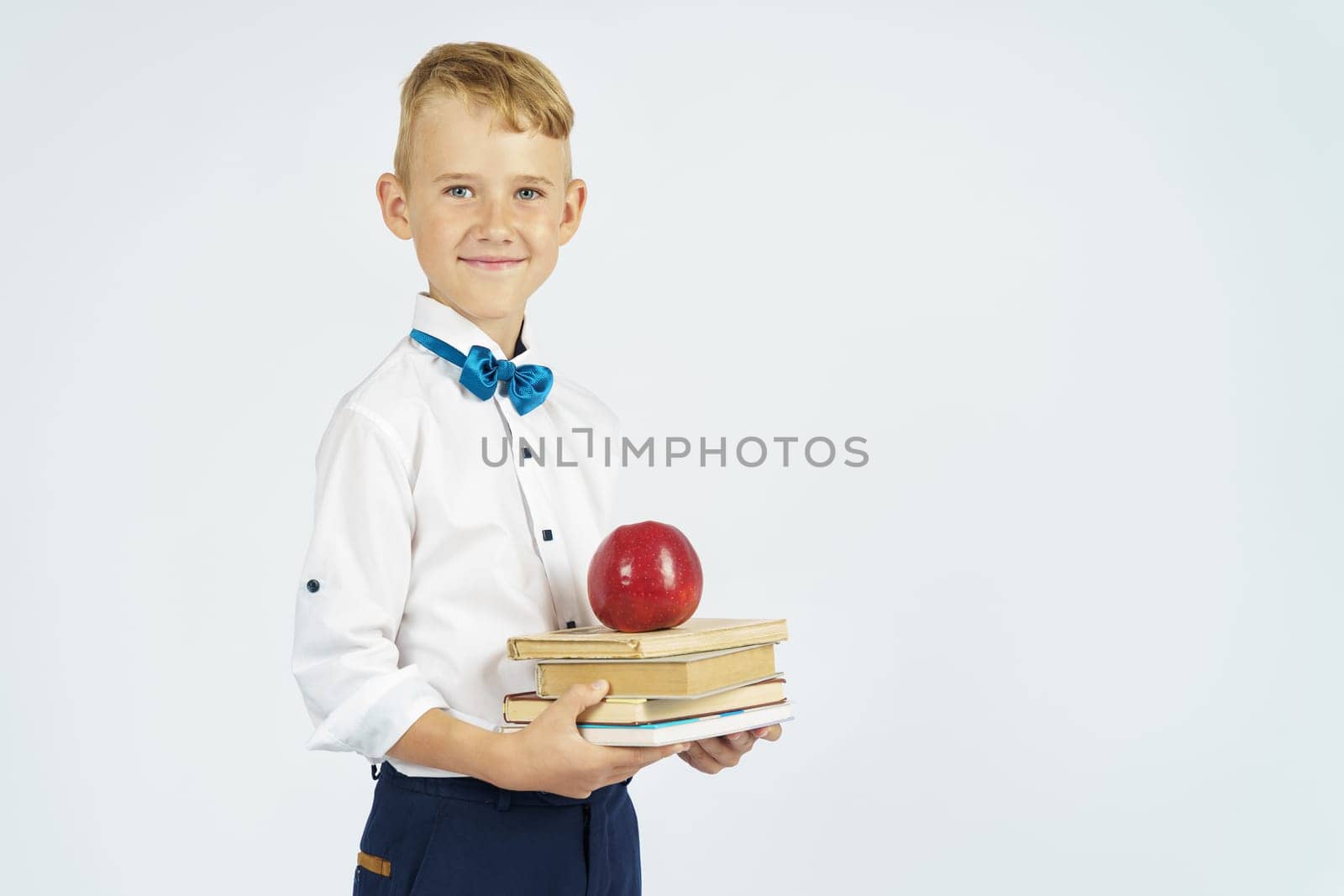 The schoolboy holds books and an apple in his hands. Isolated background. Education concept