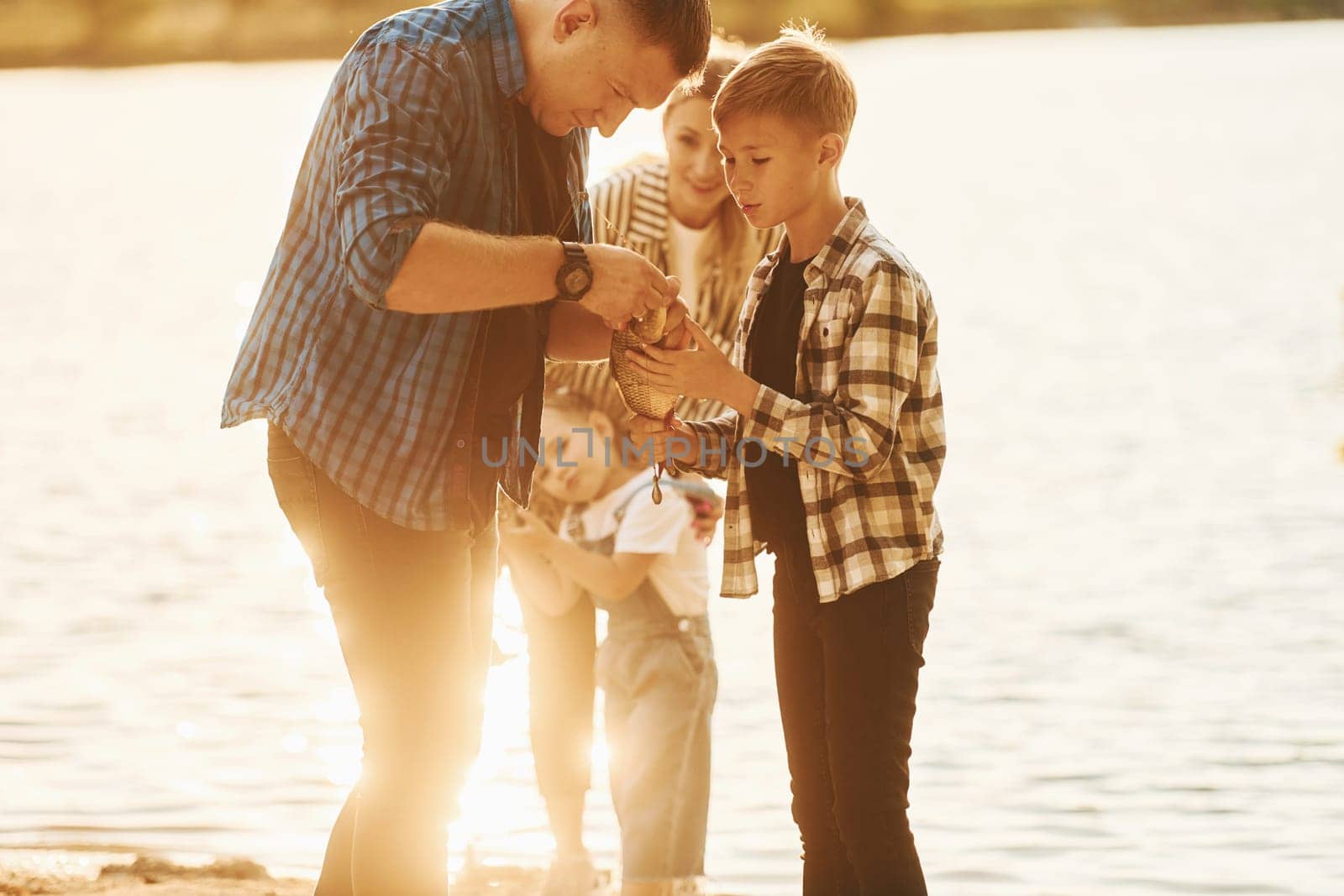 Illuminated by sunlight. Father and mother with son and daughter on fishing together outdoors at summertime by Standret