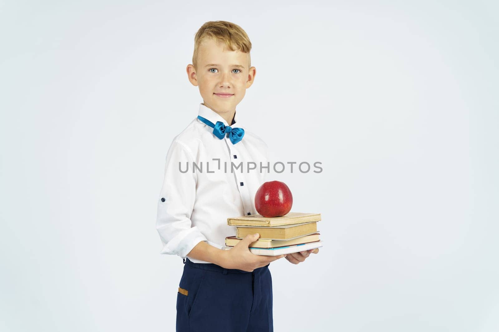 The schoolboy holds books and an apple in his hands. Isolated background. Education concept