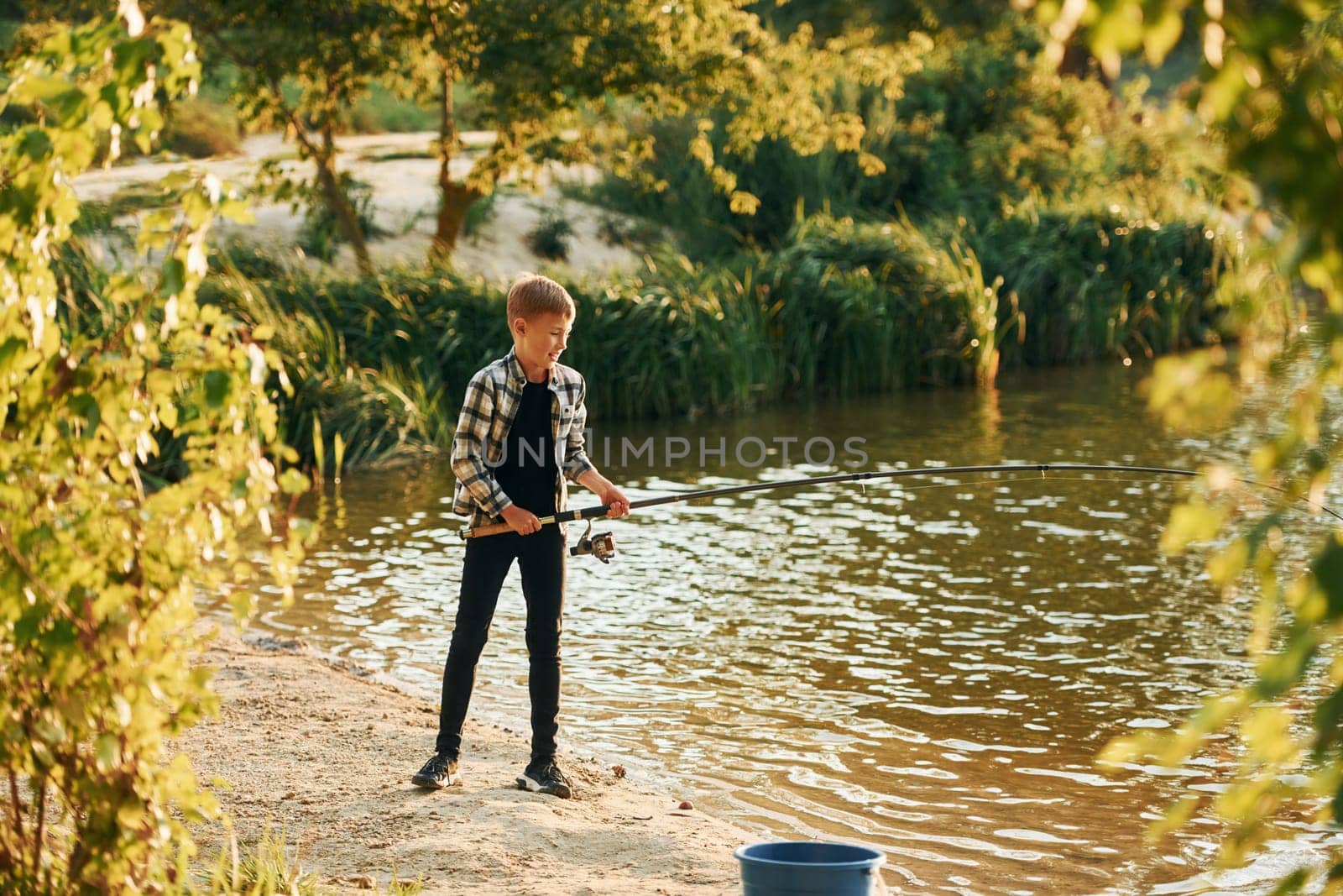 With good catch. Boy in casual clothes in on fishion outdoors at summertime.