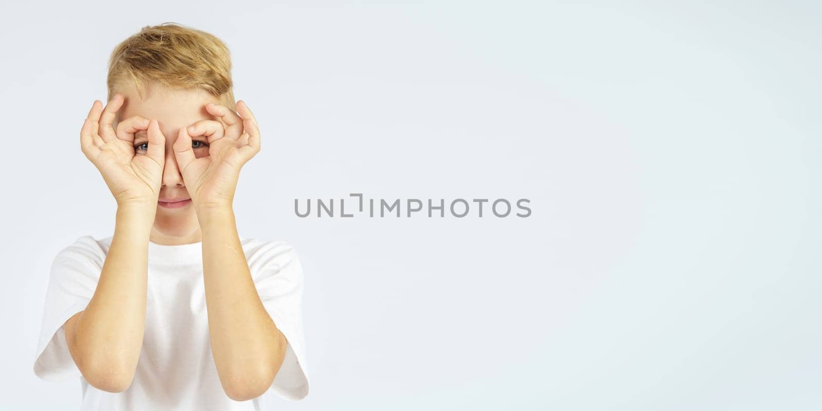 A portrait of a schoolboy who put his hands to his eyes - shows binoculars. Isolated background. Education concept.