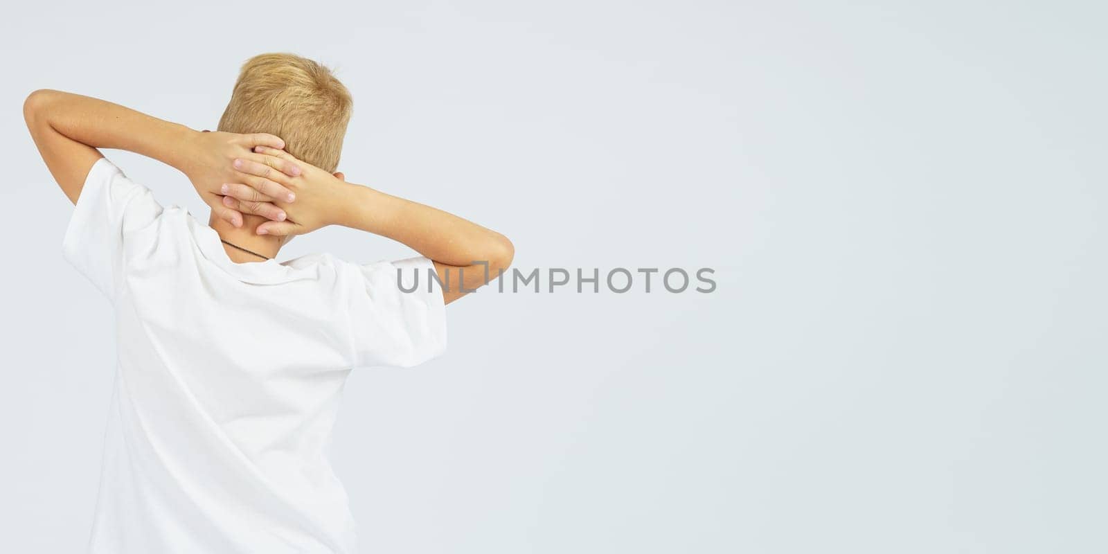 A portrait of a schoolboy who turned away from the camera and holds his hands behind his head. Isolated background. Education concept.