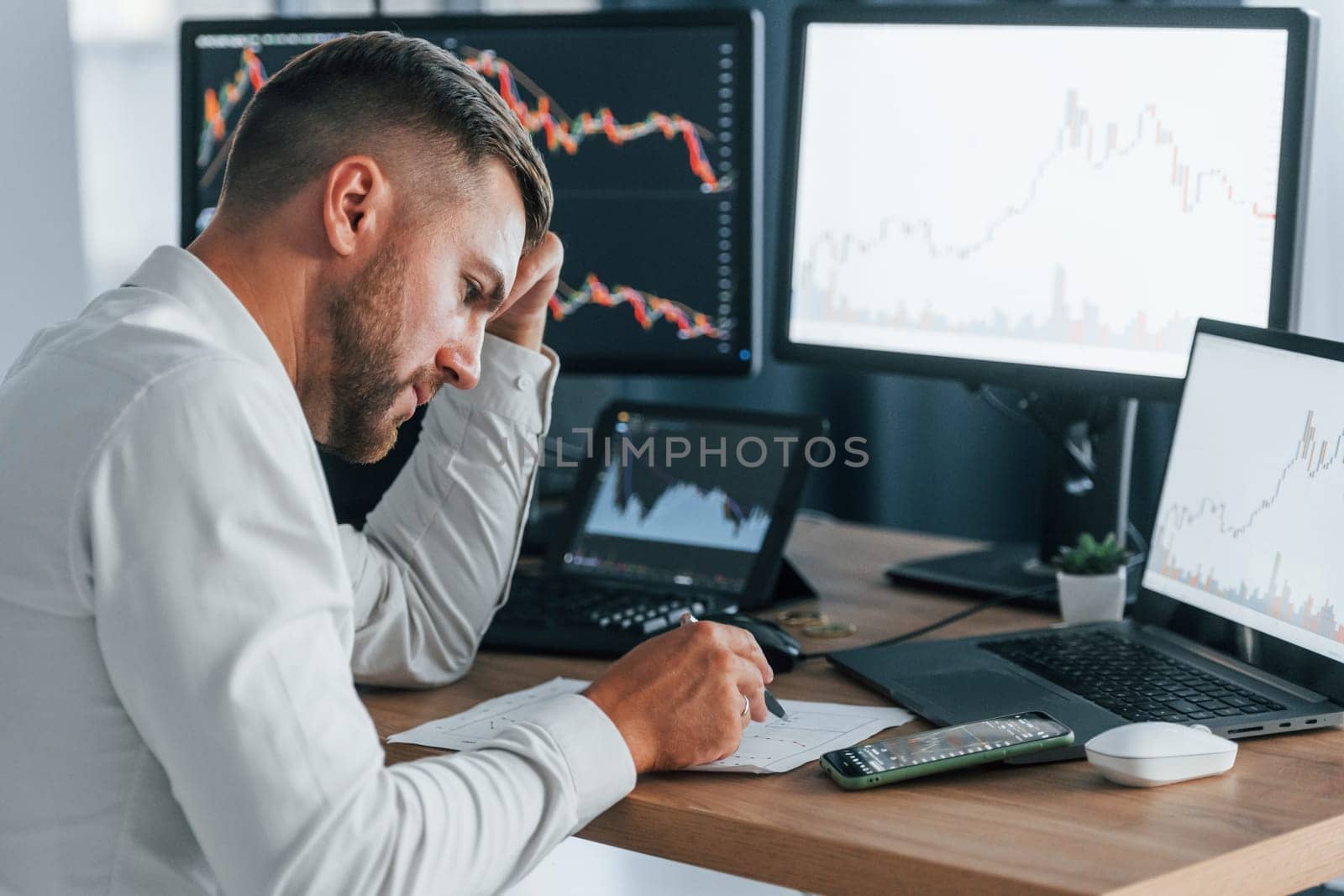 Young businessman in formal clothes is in office with multiple screens.