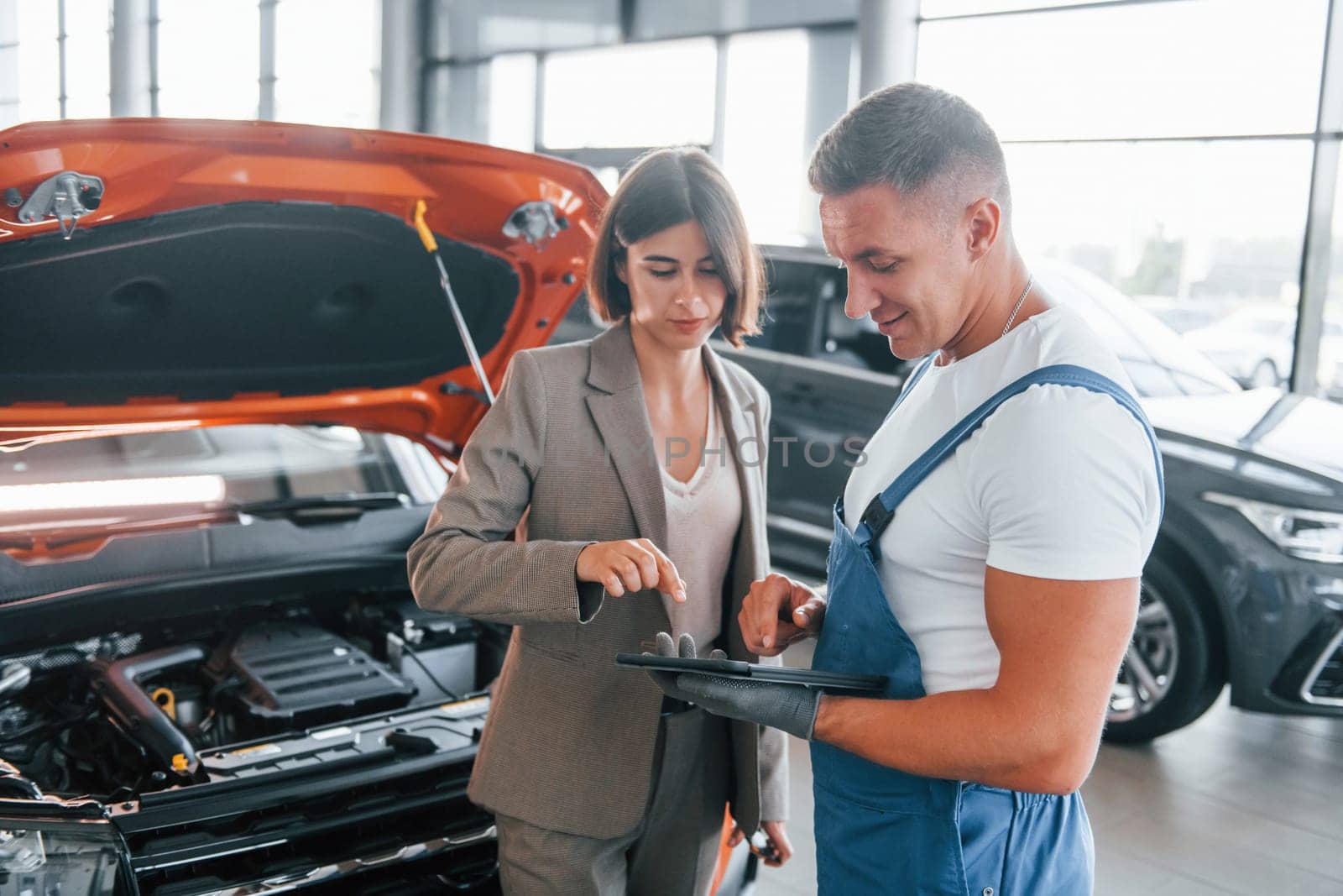 With female customer. Man repairing woman's automobile indoors. Professional service.