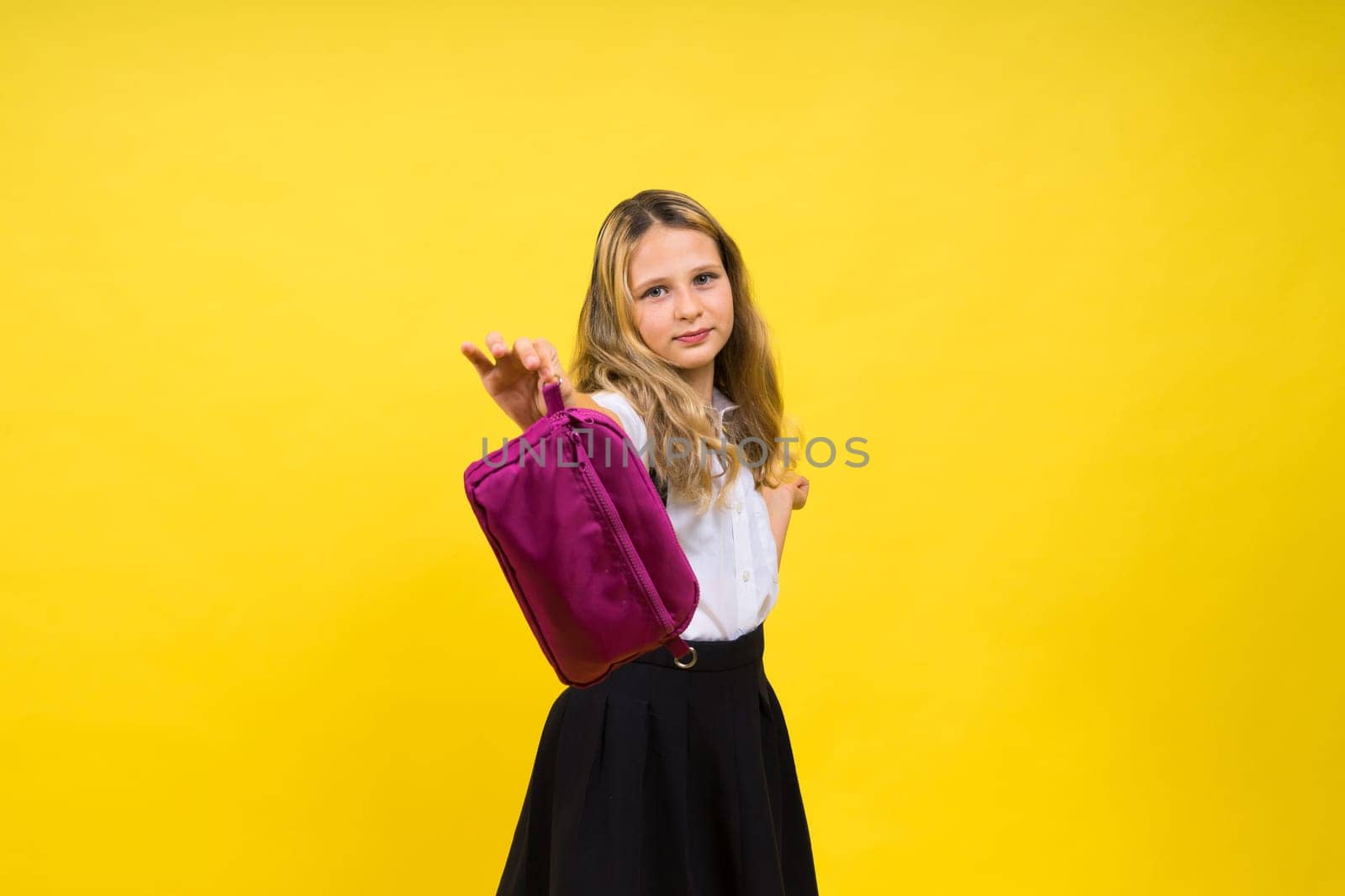 Little teenager girl with pencil case on a yellow background