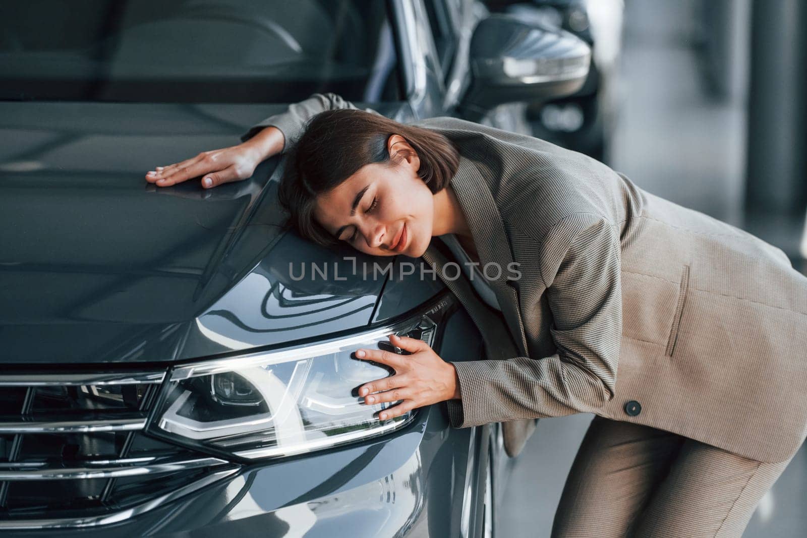 Black colored car. Woman is indoors near brand new automobile indoors.