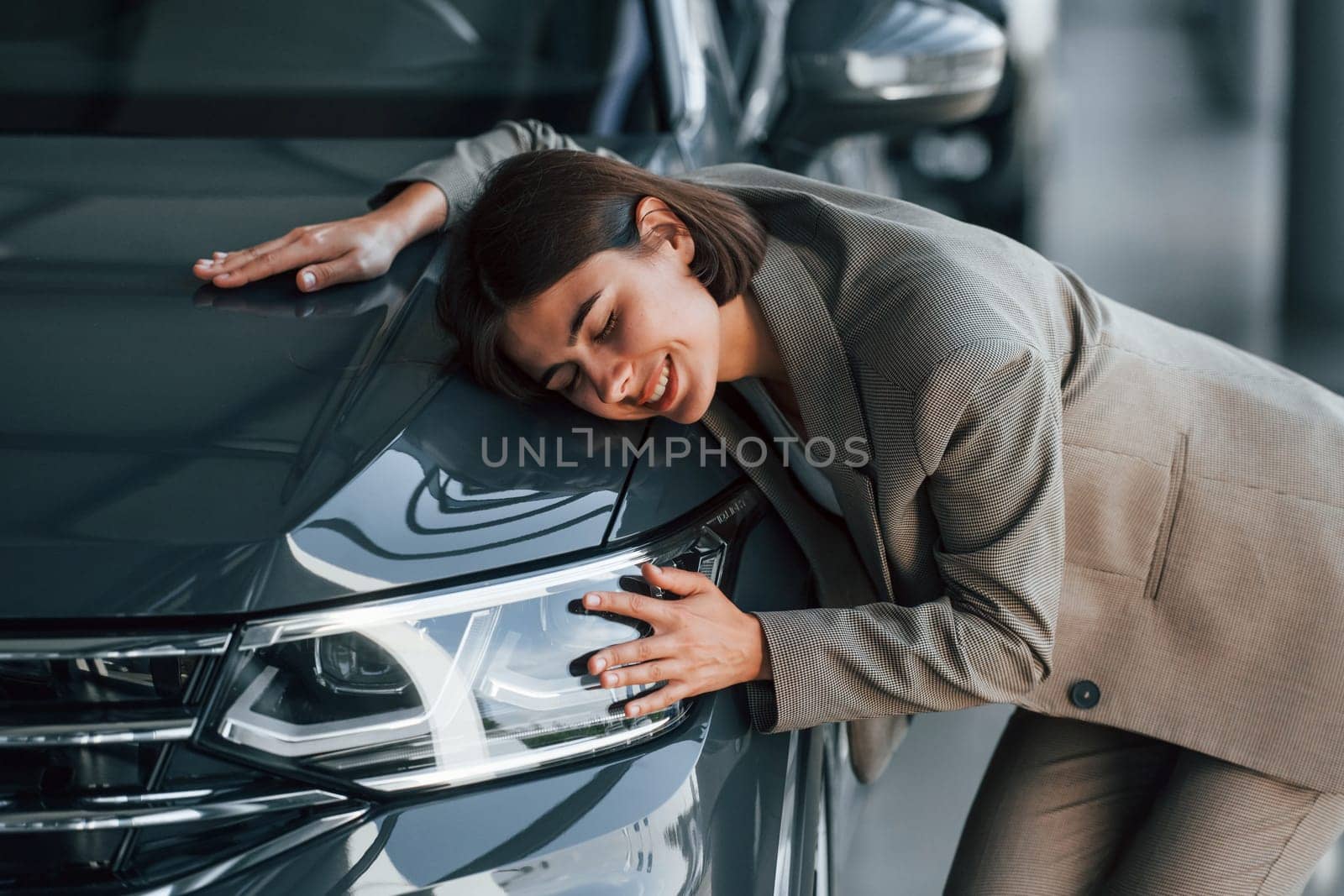 Black colored car. Woman is indoors near brand new automobile indoors.