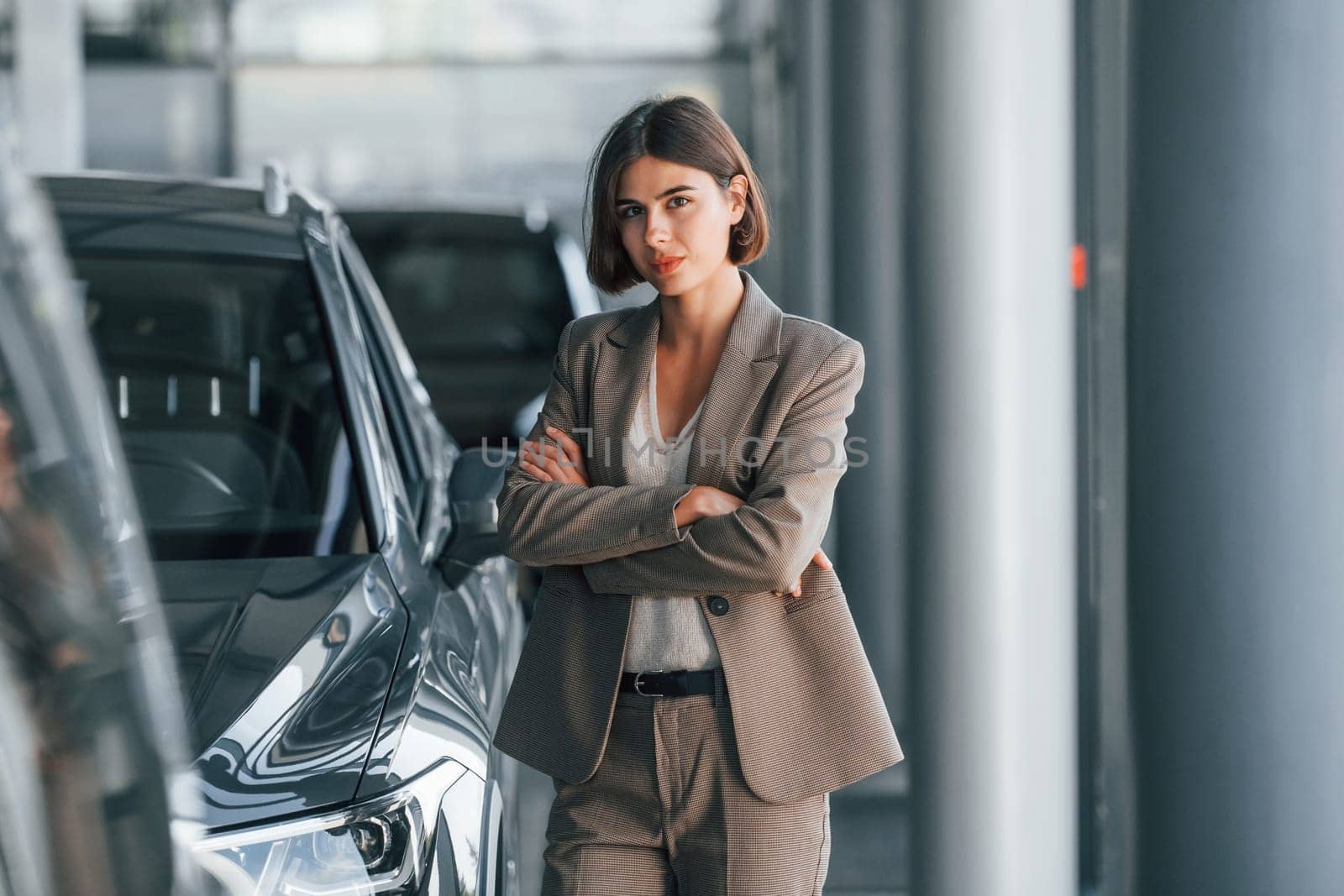 Black colored car. Woman is indoors near brand new automobile indoors.