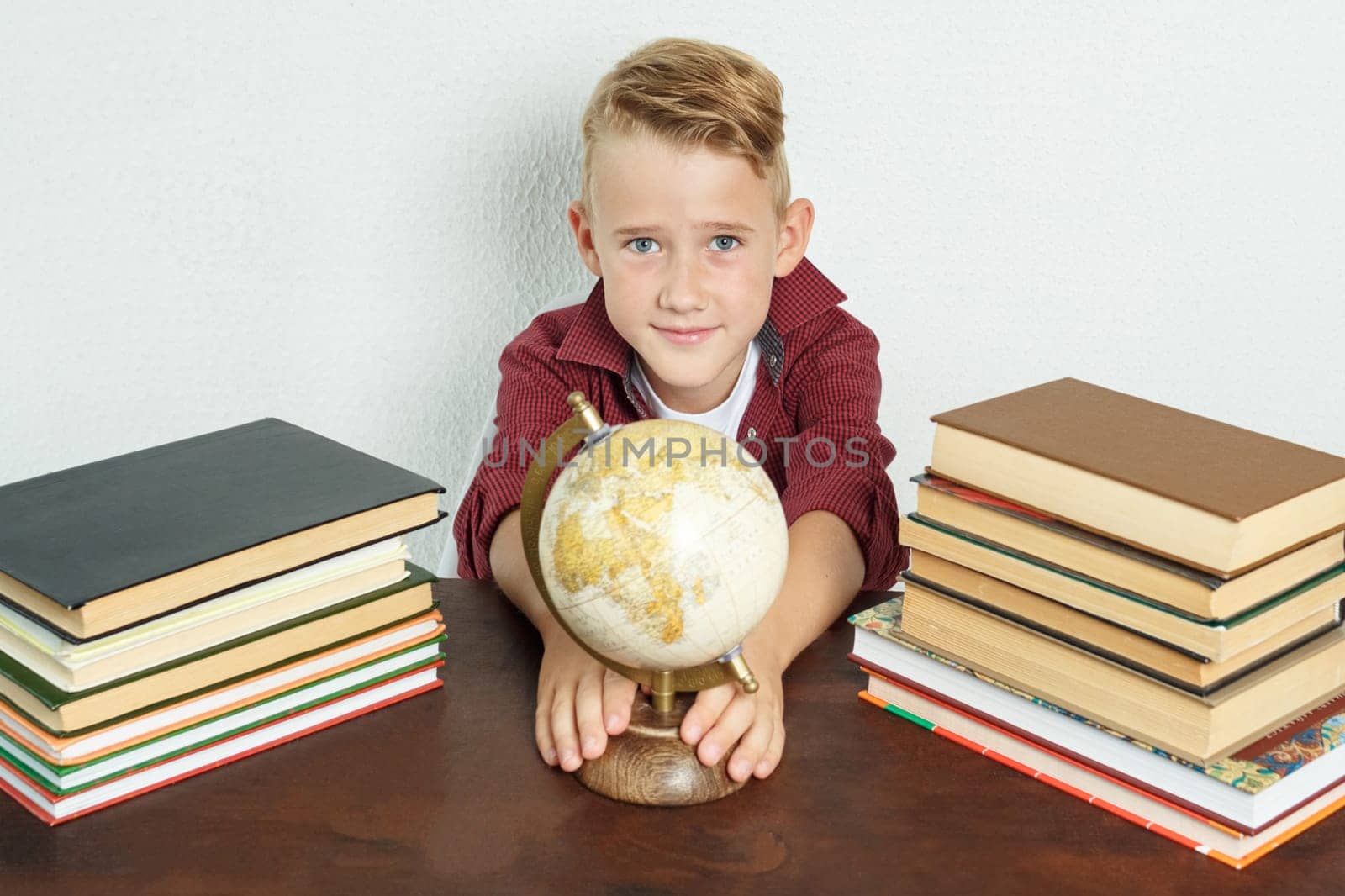 The schoolboy sits at the table, shows the globe. On the table there are books, a globe and an alarm clock. by Sd28DimoN_1976