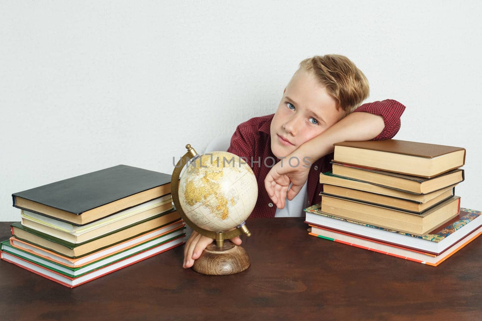 The schoolboy sits at the table, shows the globe with his elbows on the books. On the table there are books, a globe and an alarm clock. by Sd28DimoN_1976