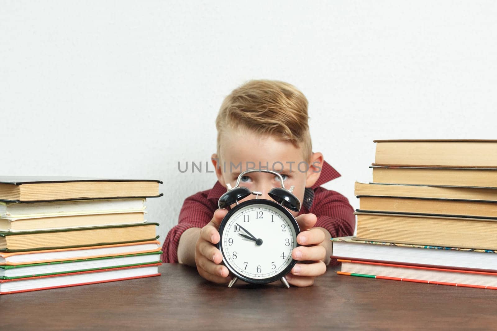 The schoolboy sits at the table and holds an alarm clock in his hands. Sharpness of the image on the alarm clock by Sd28DimoN_1976