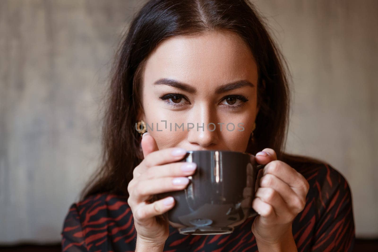 Portrait of a young woman of Caucasian appearance in a cafe with a cup of coffee. Beautiful brunette with brown eyes. Enjoying morning coffee in a cozy cafeteria