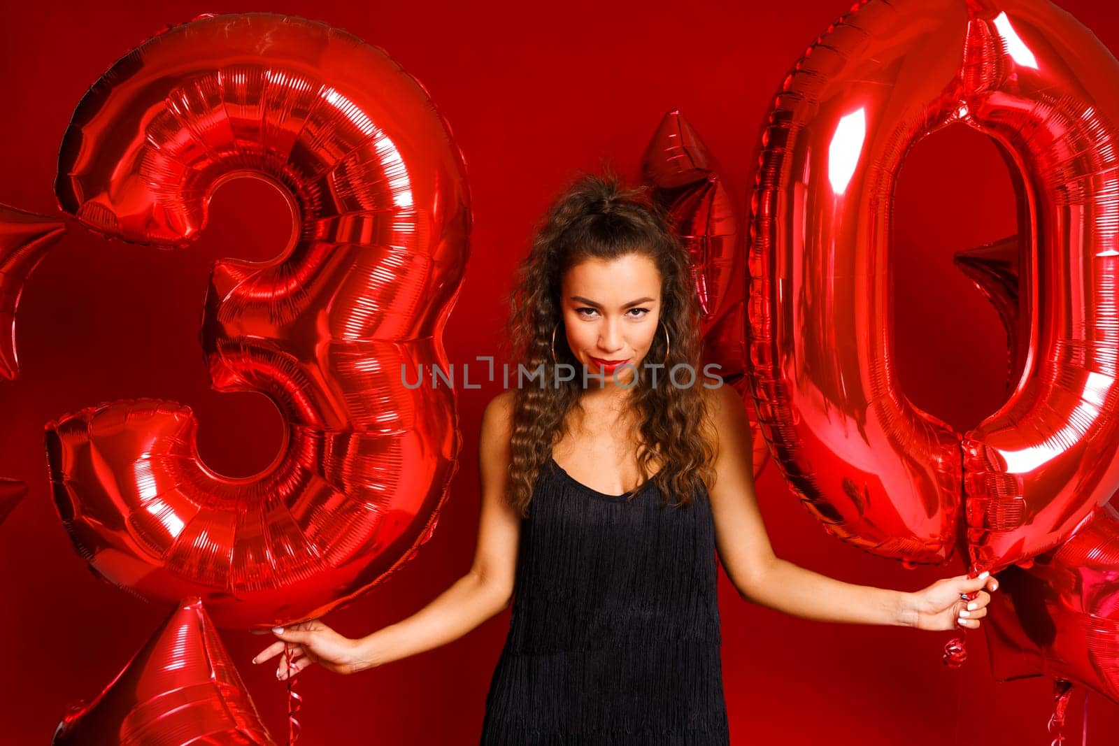 Valentine Beauty girl with red balloon. Beautiful Happy Caucasian Young woman Holiday party, birthday. Joyful model - Image. On a red background, red balloons in the form of numbers 30