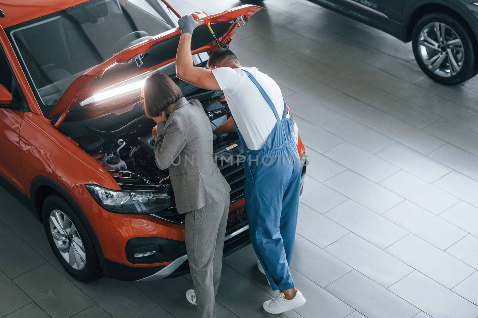 Owner standing near the man that repairing automobile indoors. Professional service.