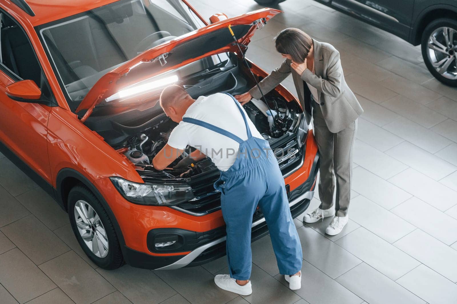 Owner standing near the man that repairing automobile indoors. Professional service.