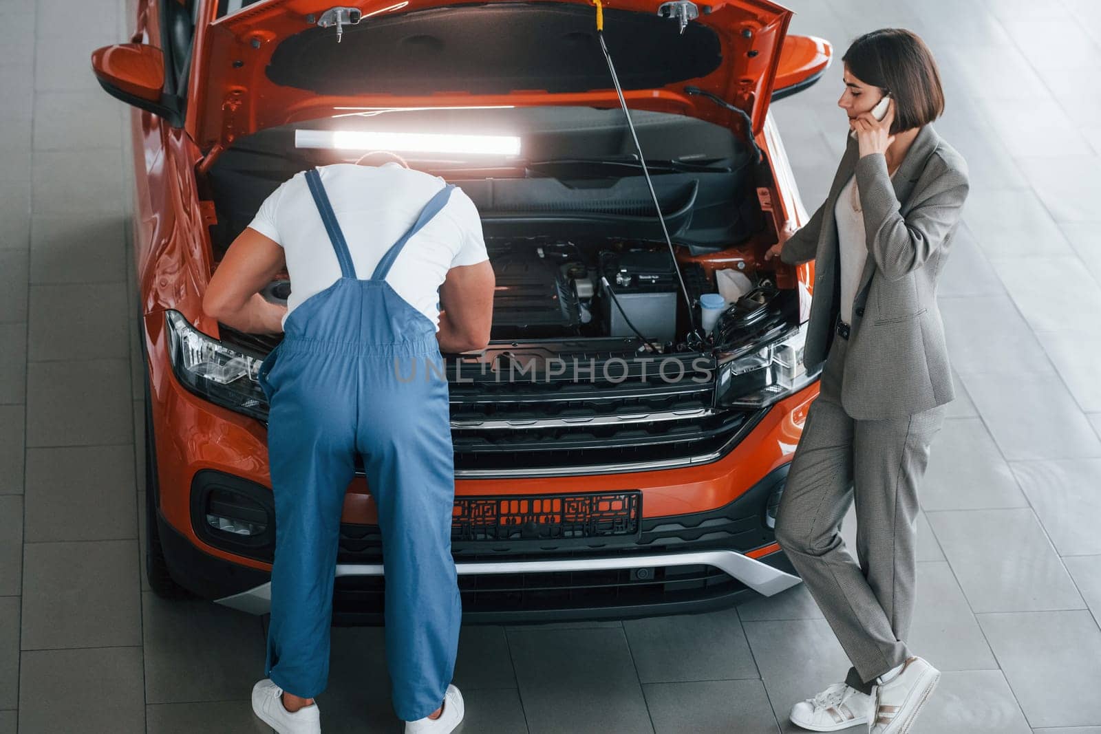 Owner standing near the man that repairing automobile indoors. Professional service.