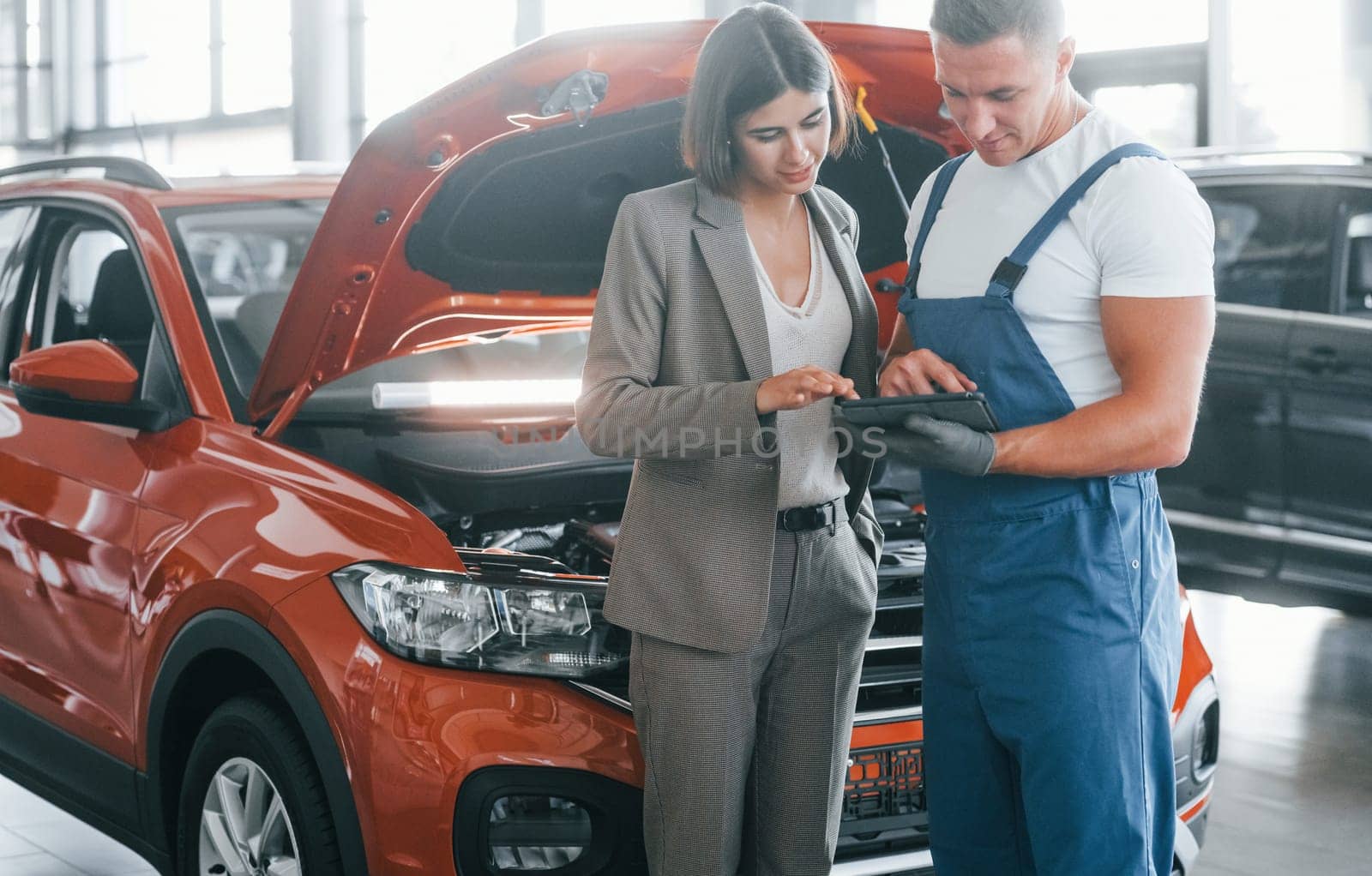 Woman in stylish clothes. Man repairing woman's automobile indoors. Professional service.